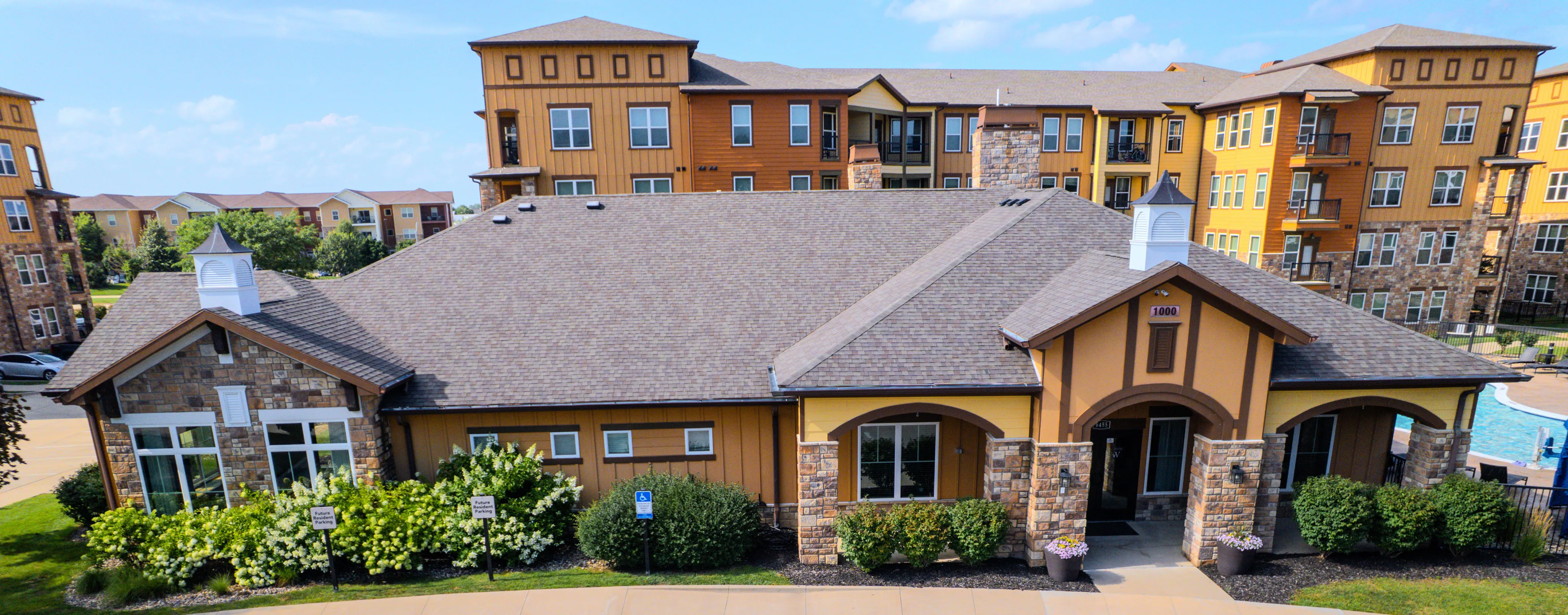 Charming apartment complex with elegant stonework and inviting pool area, surrounded by lush greenery and modern amenities.