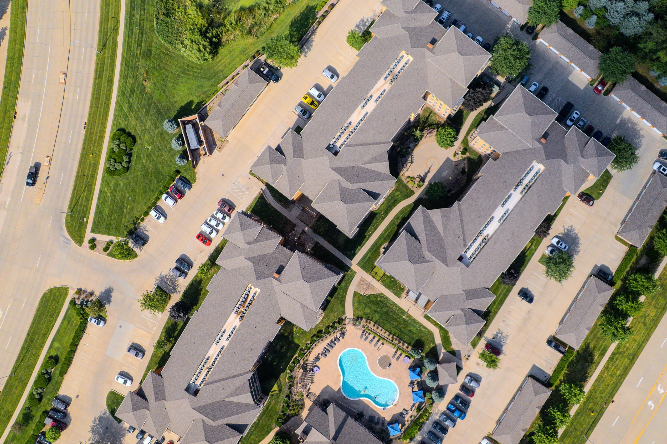 Aerial view of a modern apartment complex featuring lush greenery, ample parking, and a central pool area.
