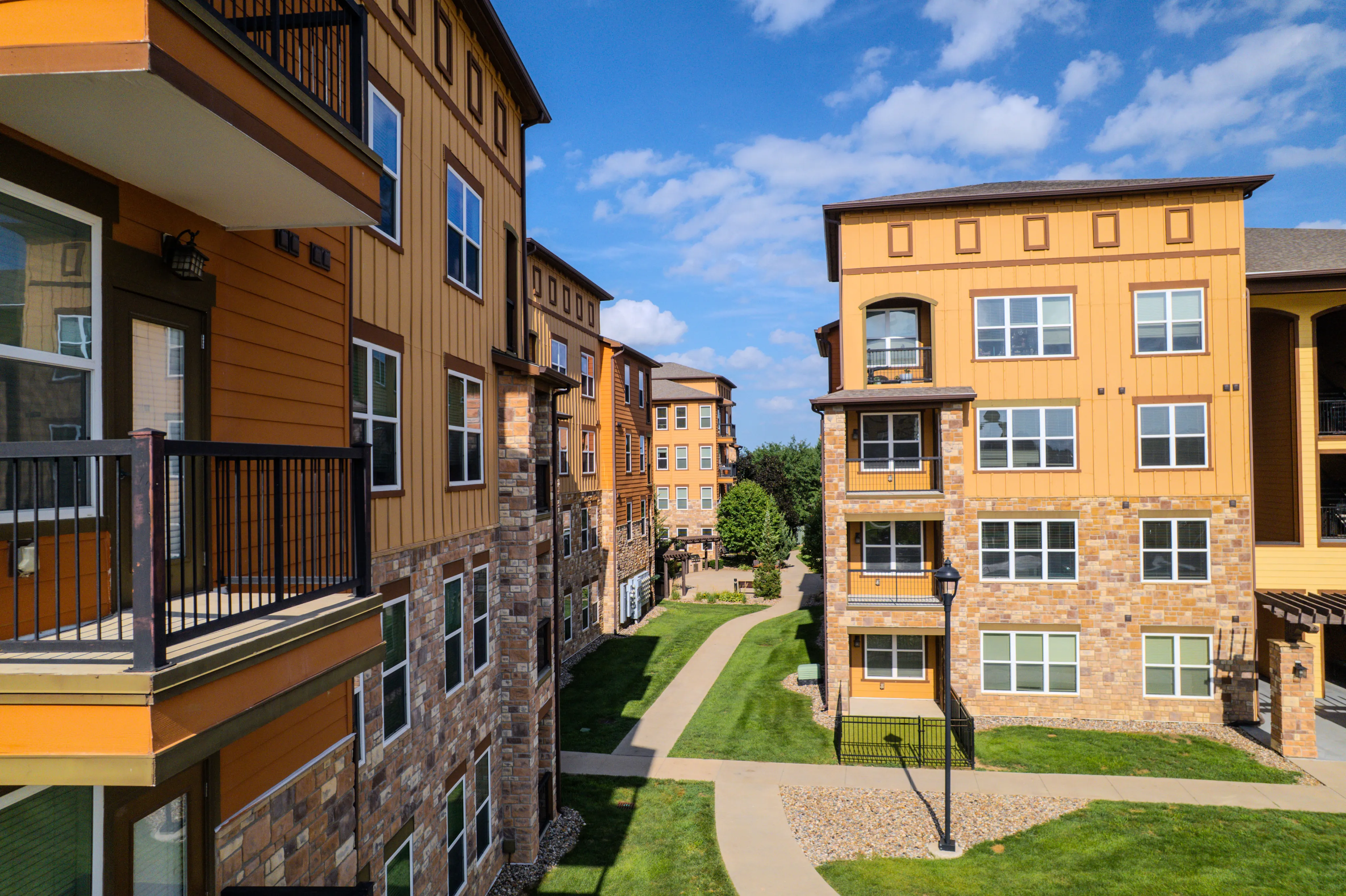 Charming apartment complex showcasing warm-toned exterior, lush green paths, and inviting balconies beneath a clear blue sky.
