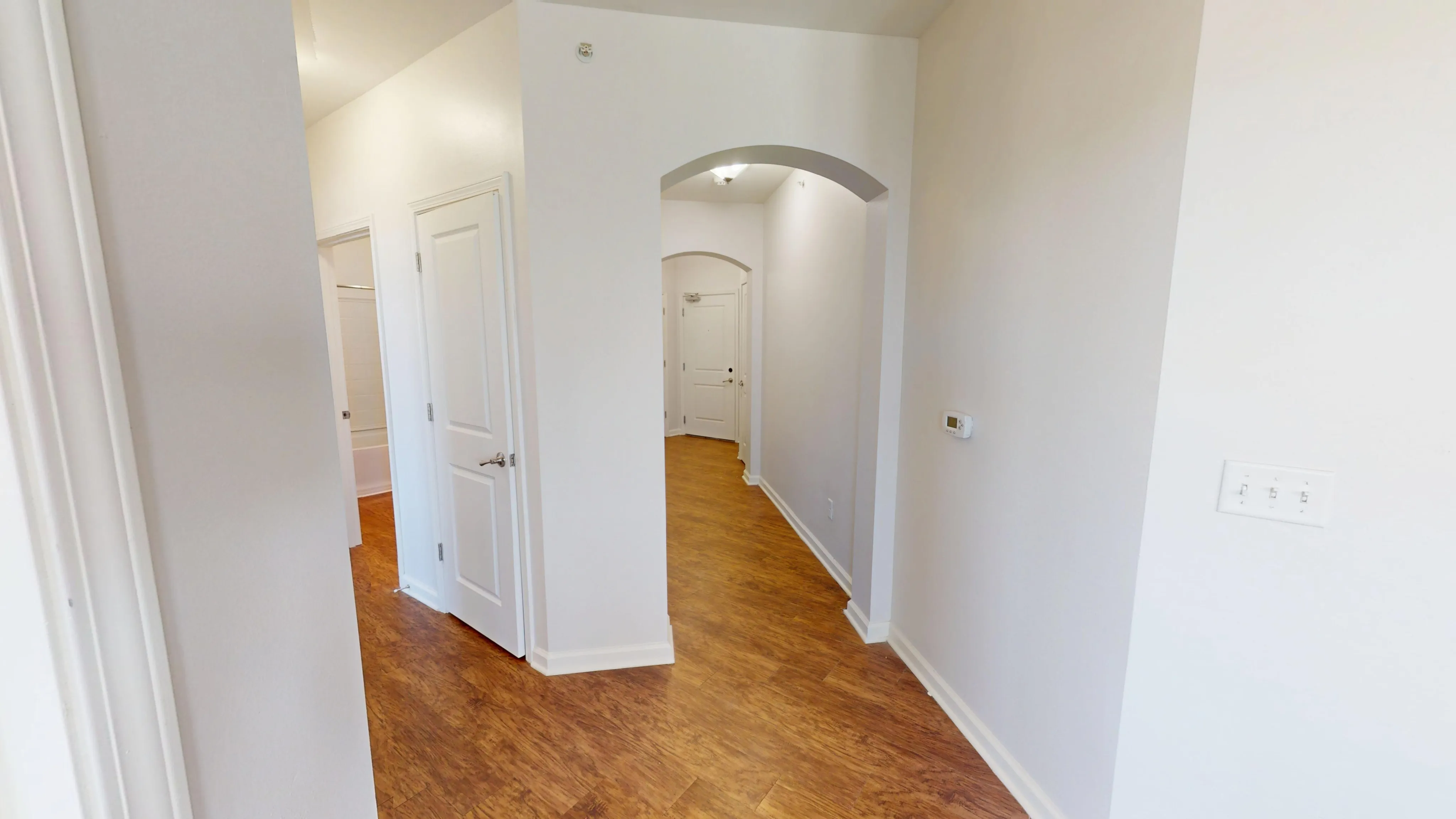 Inviting hallway with warm wooden flooring leading to pristine white doors and archways, showcasing modern apartment elegance.
