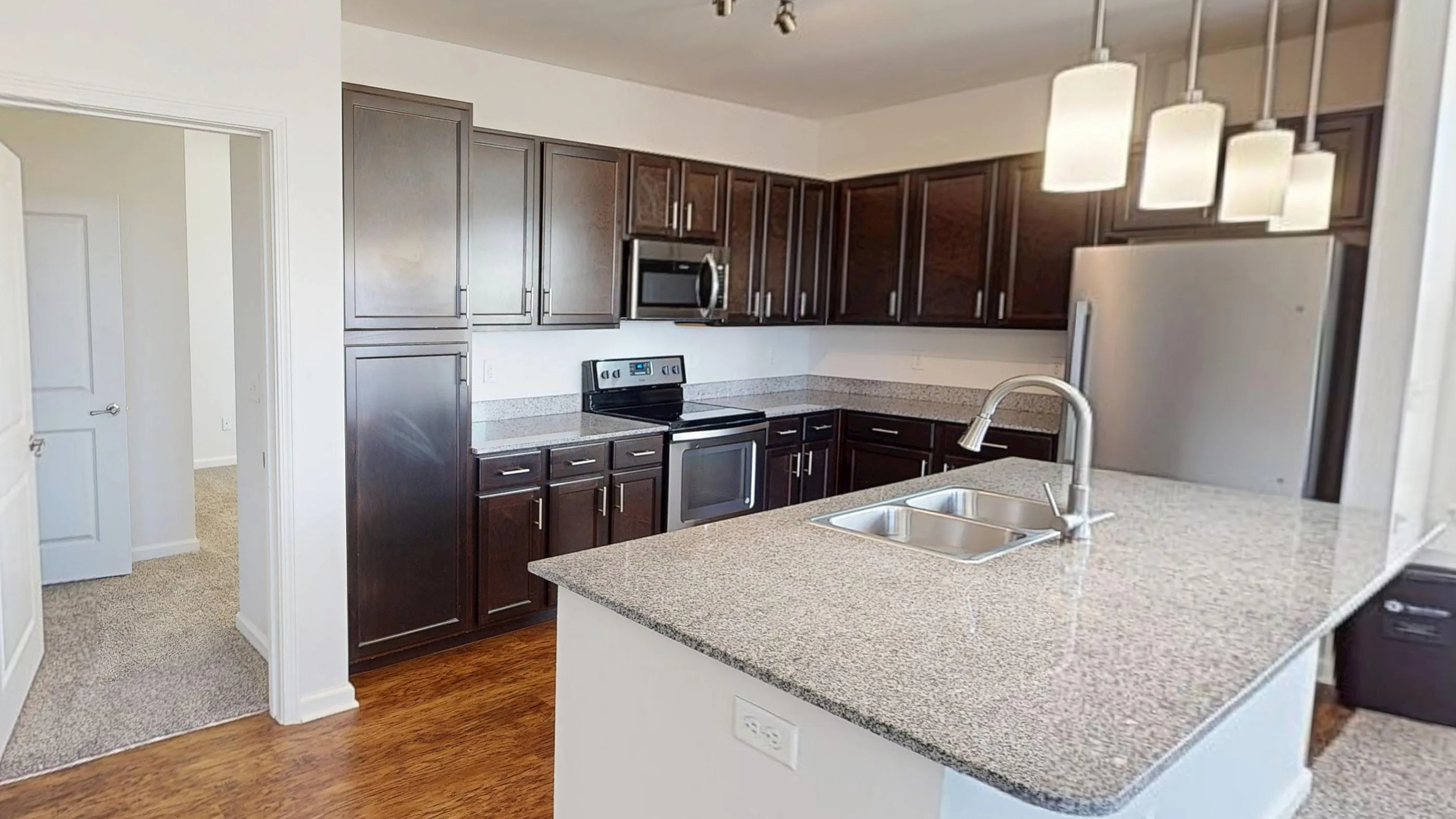 Modern kitchen with elegant dark wood cabinets, sleek granite countertops, and stainless steel appliances, highlighting a bright and welcoming open-design space.