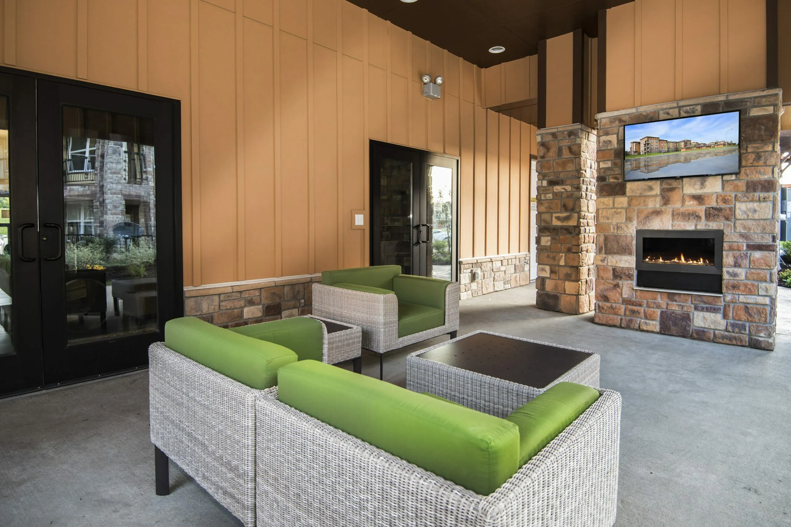 Chic outdoor lounge area featuring modern wicker seating with green cushions, a cozy stone fireplace, and elegant architectural elements.