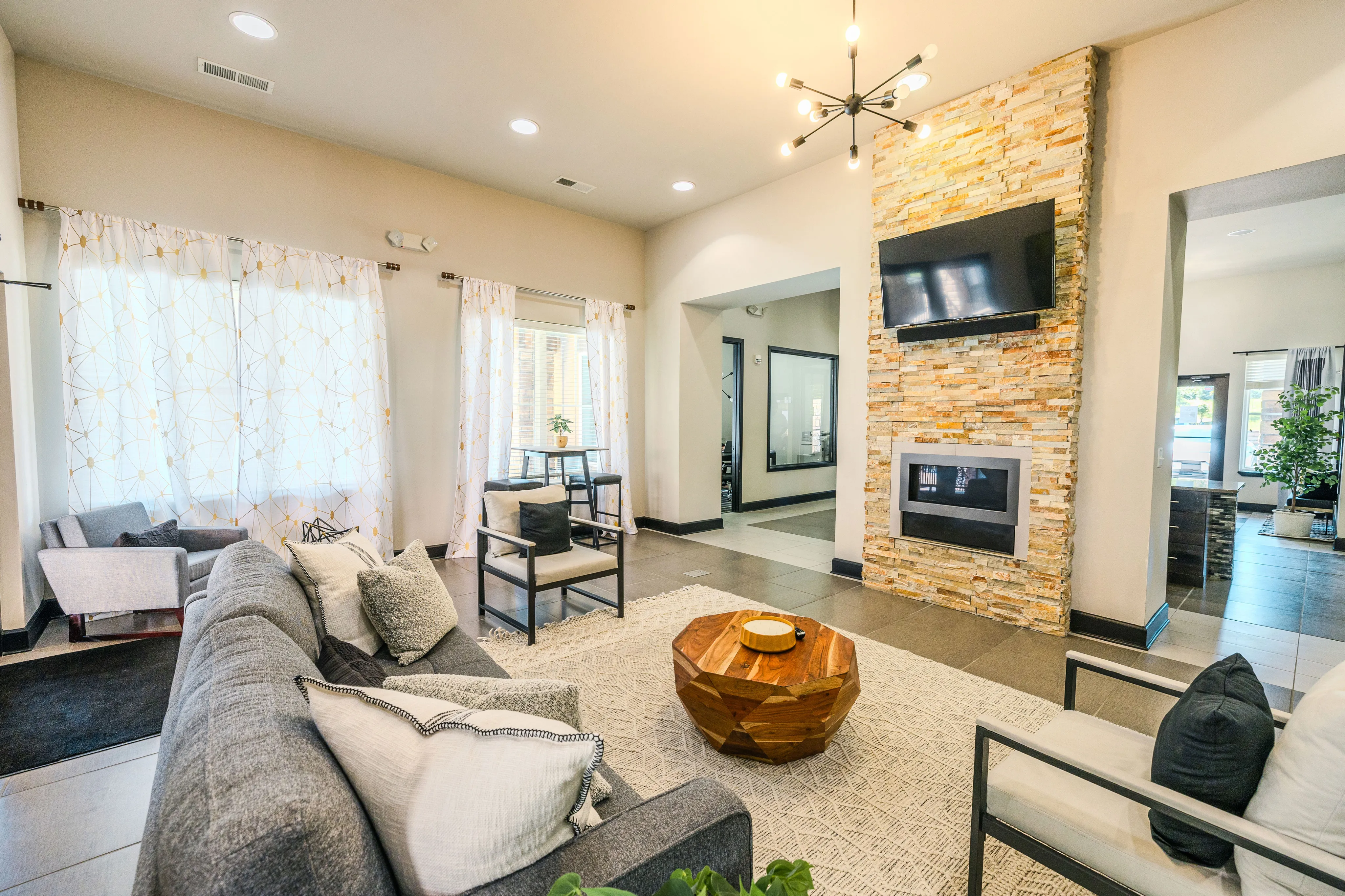Inviting living room featuring a modern sofa, elegant light fixture, and a stylish stone fireplace with a mounted TV.