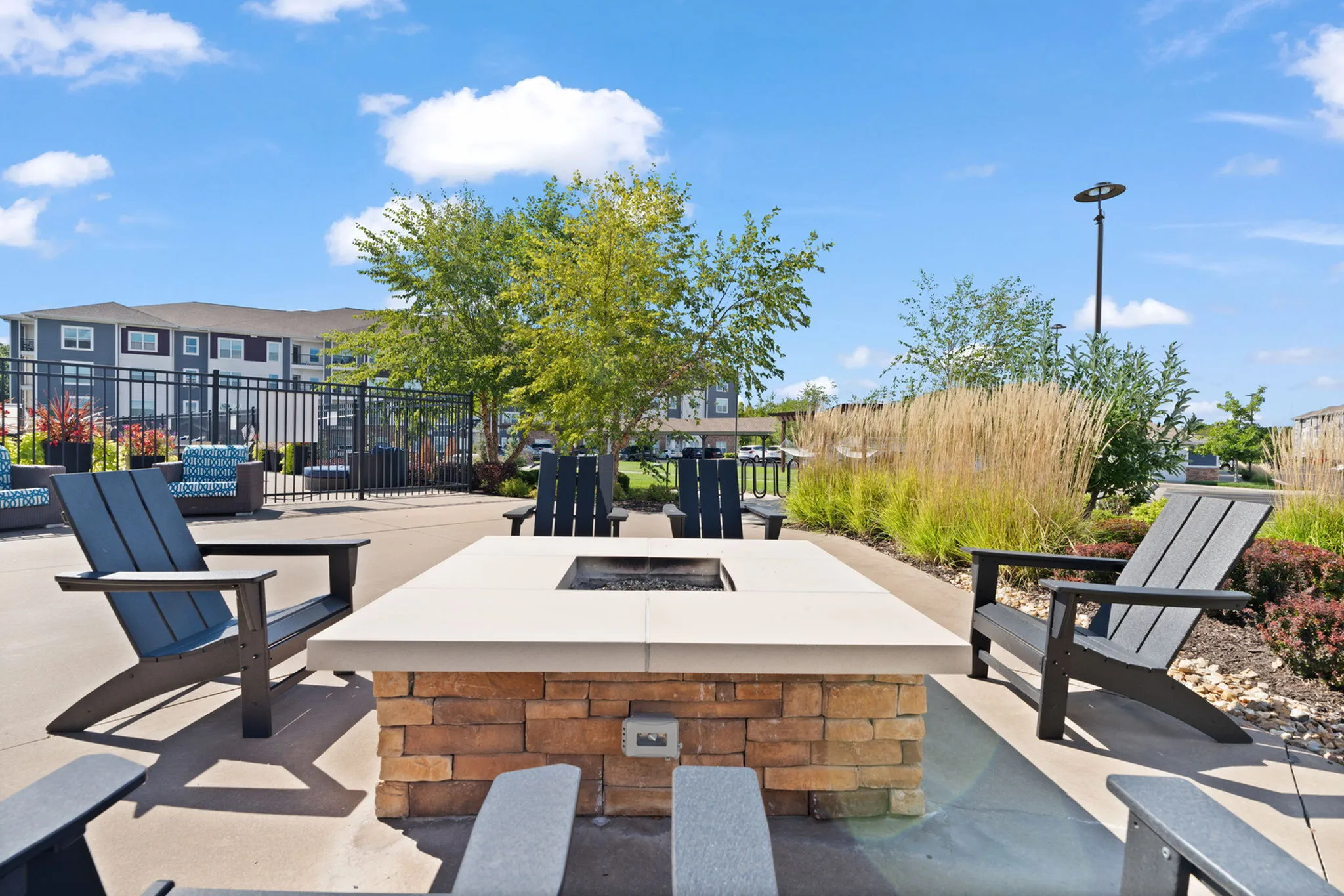 Inviting outdoor patio with stylish chairs around a cozy fire pit, surrounded by lush greenery and a clear blue sky.