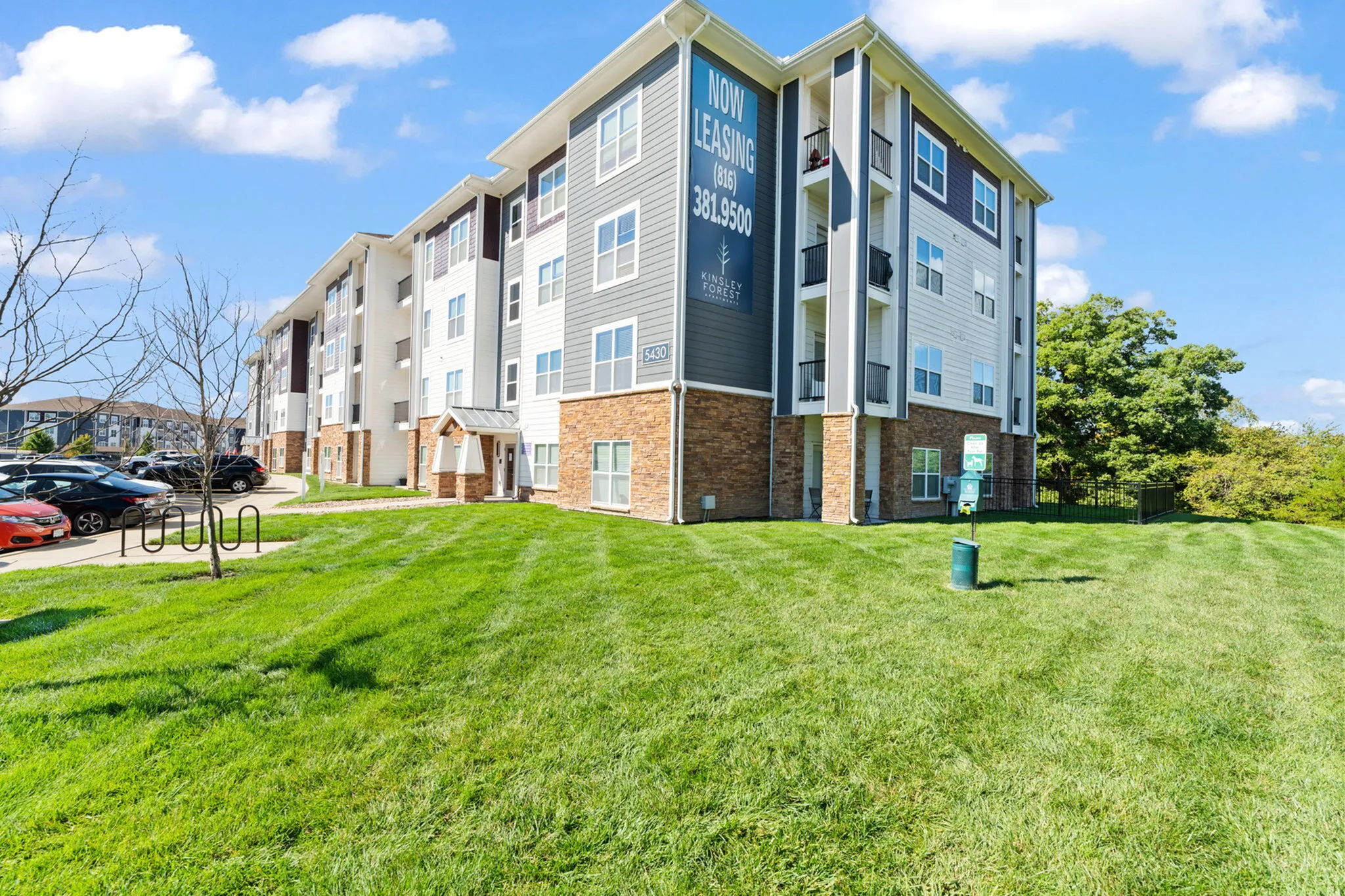 Bright and modern apartment building with lush green lawns and ample parking space, offering now leasing opportunities in a vibrant community.
