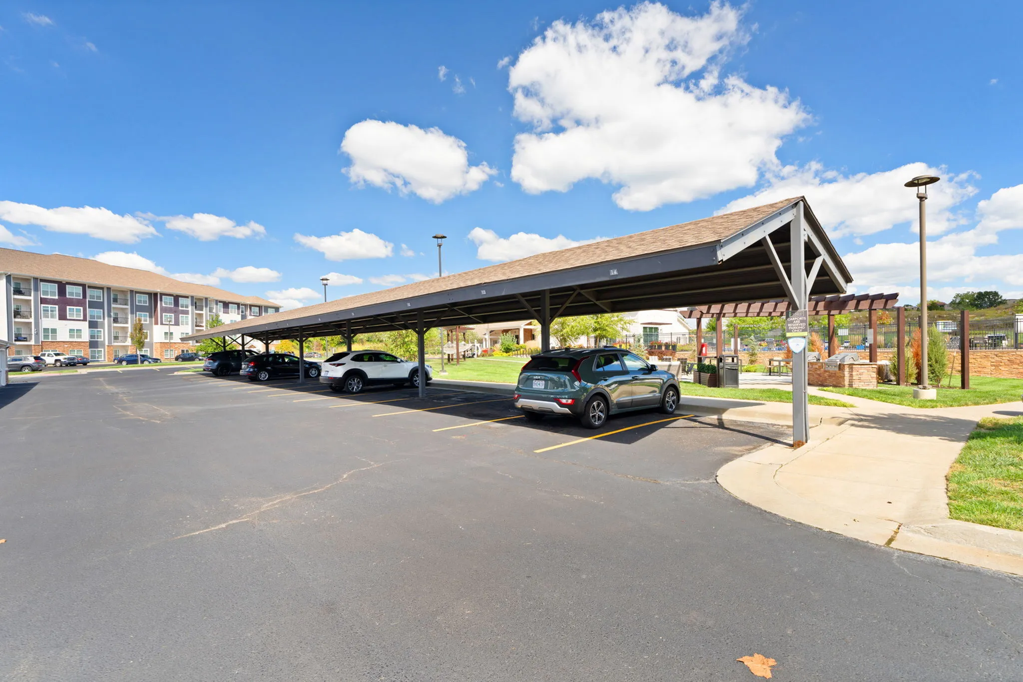 Modern apartment complex with covered parking, vibrant landscaping, and sunny weather.