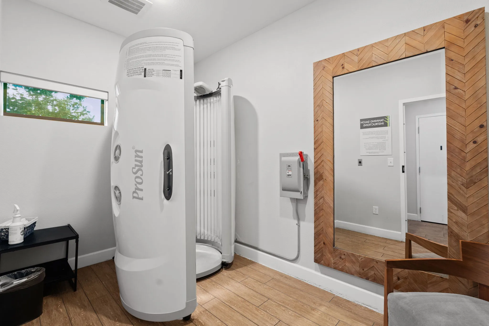Modern apartment tanning room with sleek ProSun tanning booth, stylish wooden floor, and elegant wall mirror.