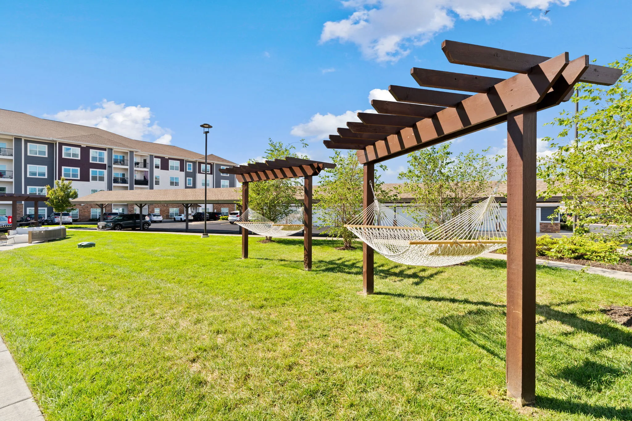 Elegant apartment complex with inviting garden area featuring wooden pergolas and relaxing hammocks, perfect for outdoor leisure.