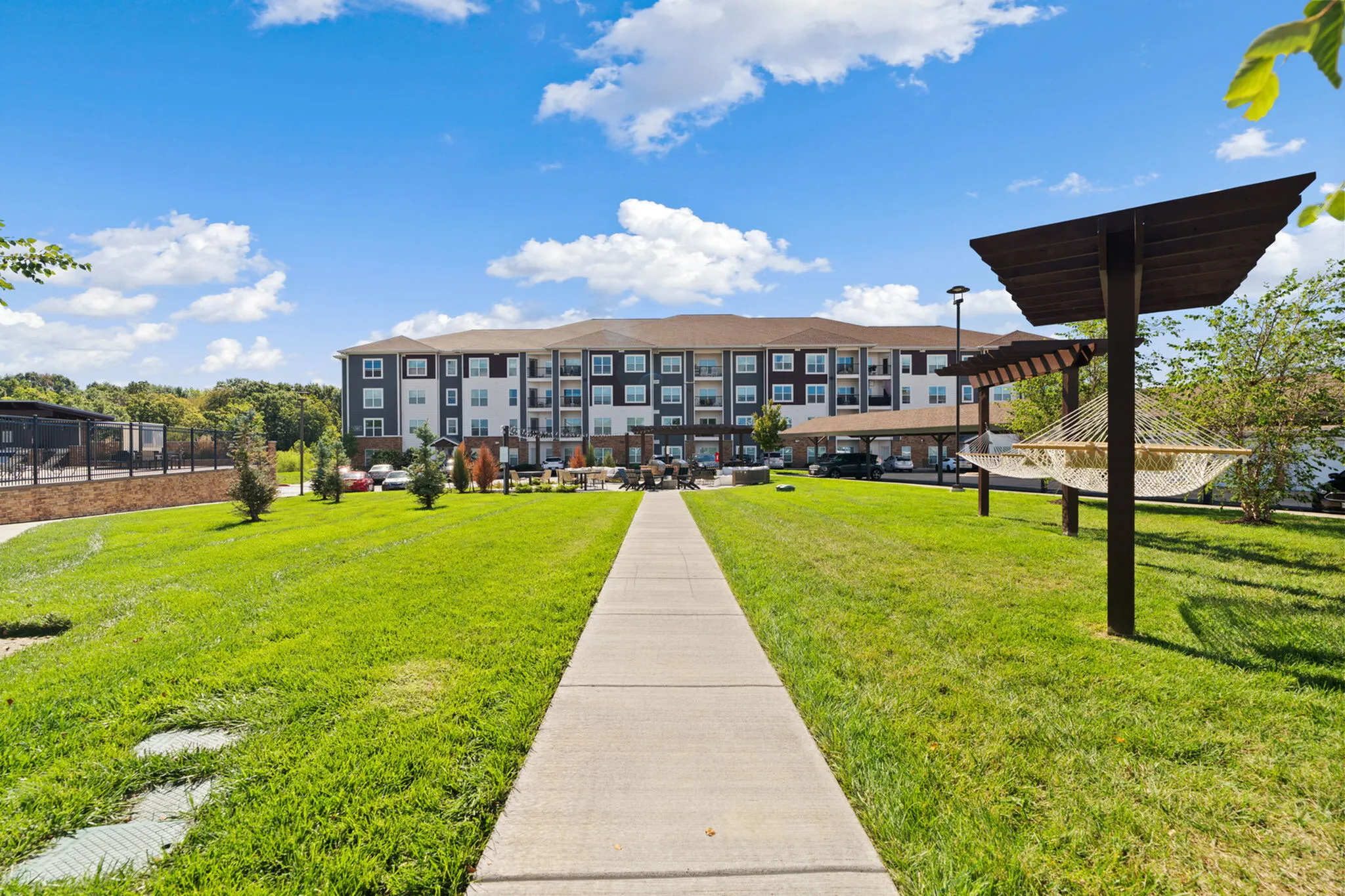 Inviting apartment complex with lush green lawns, modern architecture, and relaxing hammocks under pergolas.