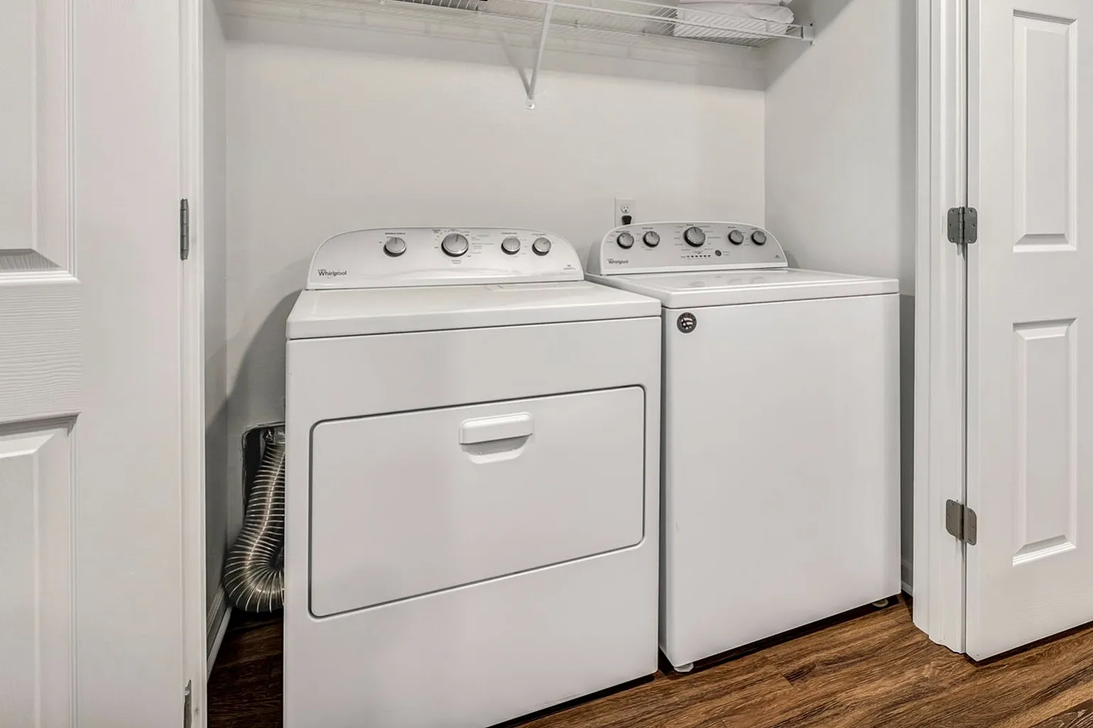 Modern laundry area featuring a sleek washer and dryer set, accented by a spacious white interior and elegant hardwood flooring.