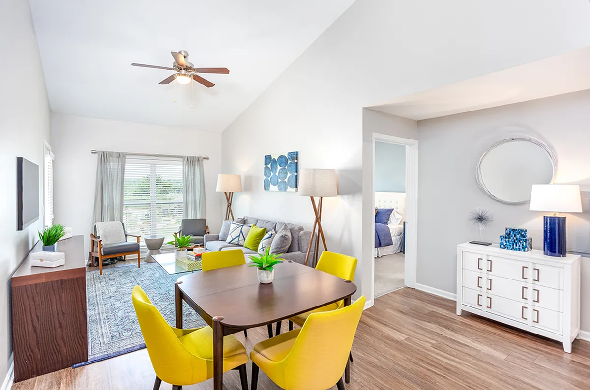 Bright, modern living area with stylish decor, featuring a cozy seating arrangement, vibrant yellow chairs, and a welcoming dining space, offering a glimpse into the tranquil bedroom.