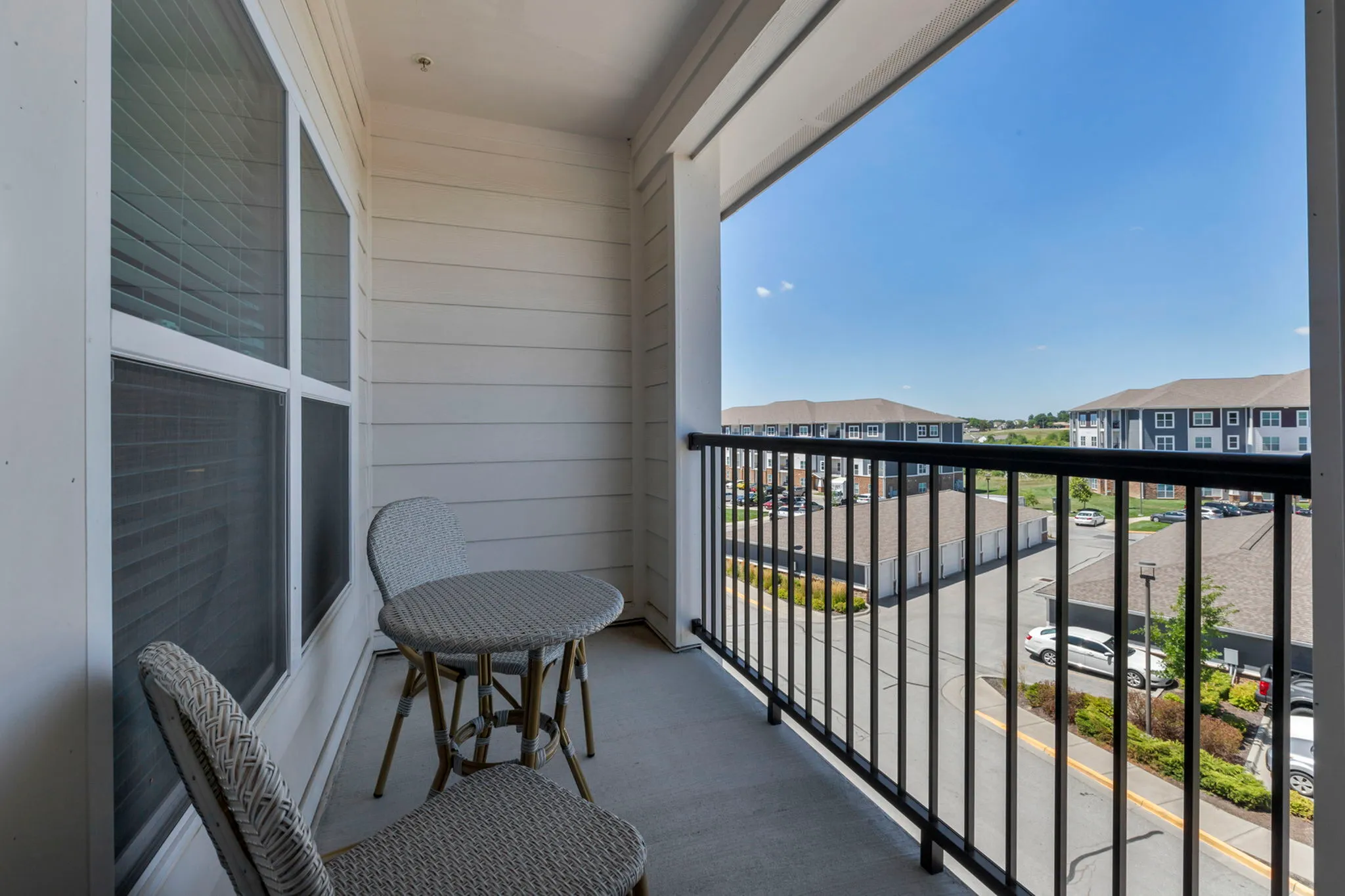 Charming apartment balcony with cozy wicker seating and a picturesque view of modern buildings under a bright blue sky.