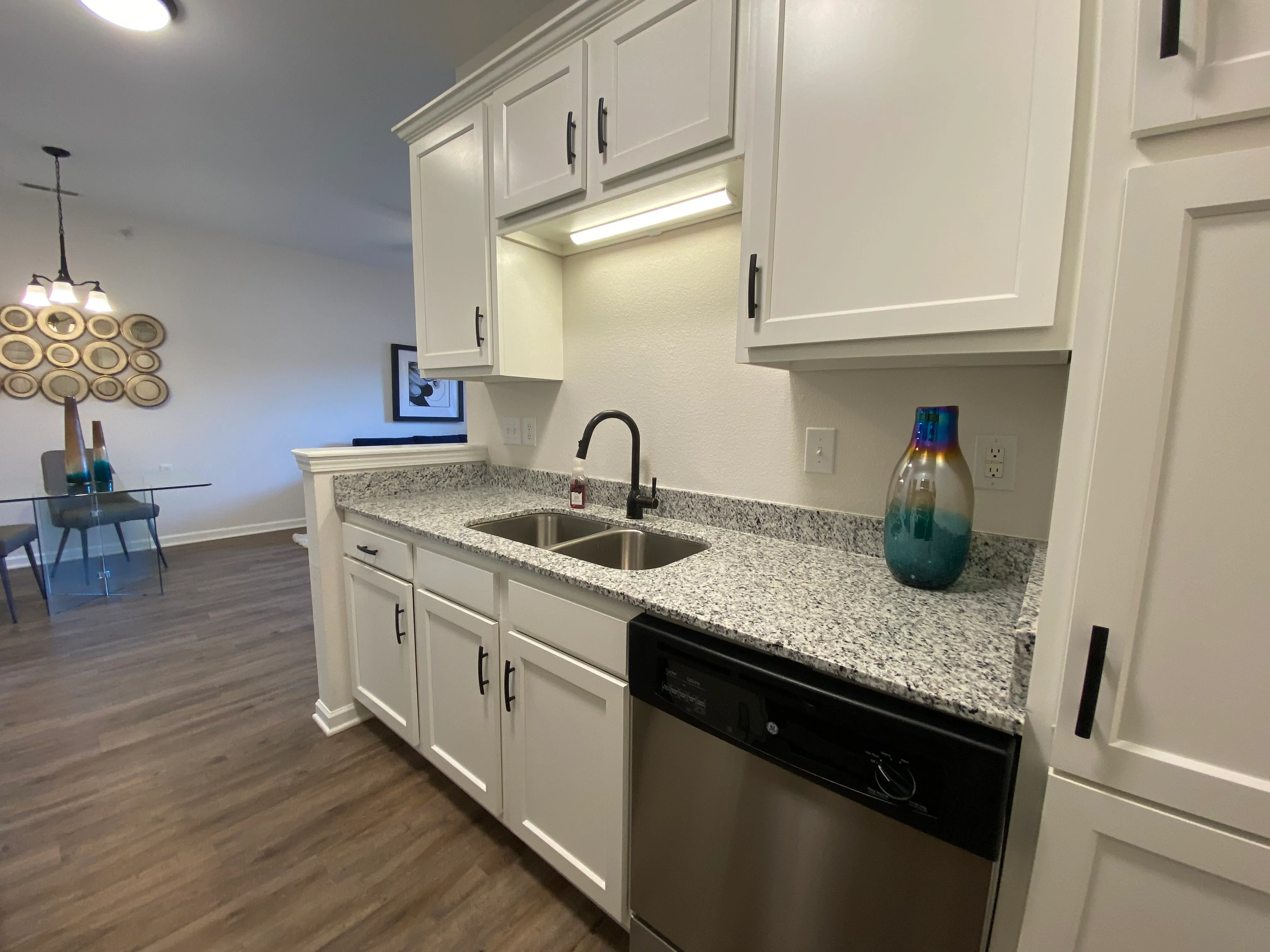 Modern kitchen with sleek white cabinets, granite countertops, and stainless steel appliances, seamlessly flowing into an elegant dining area.