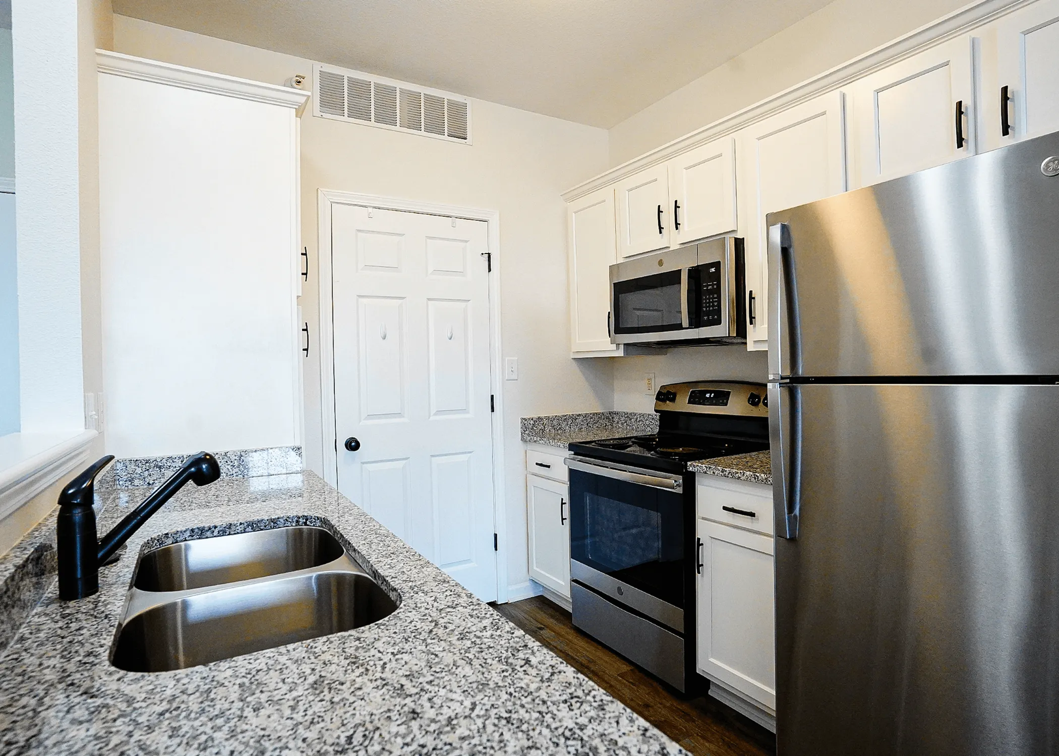 Modern kitchen boasting sleek granite countertops, stainless steel appliances, and stylish white cabinetry.