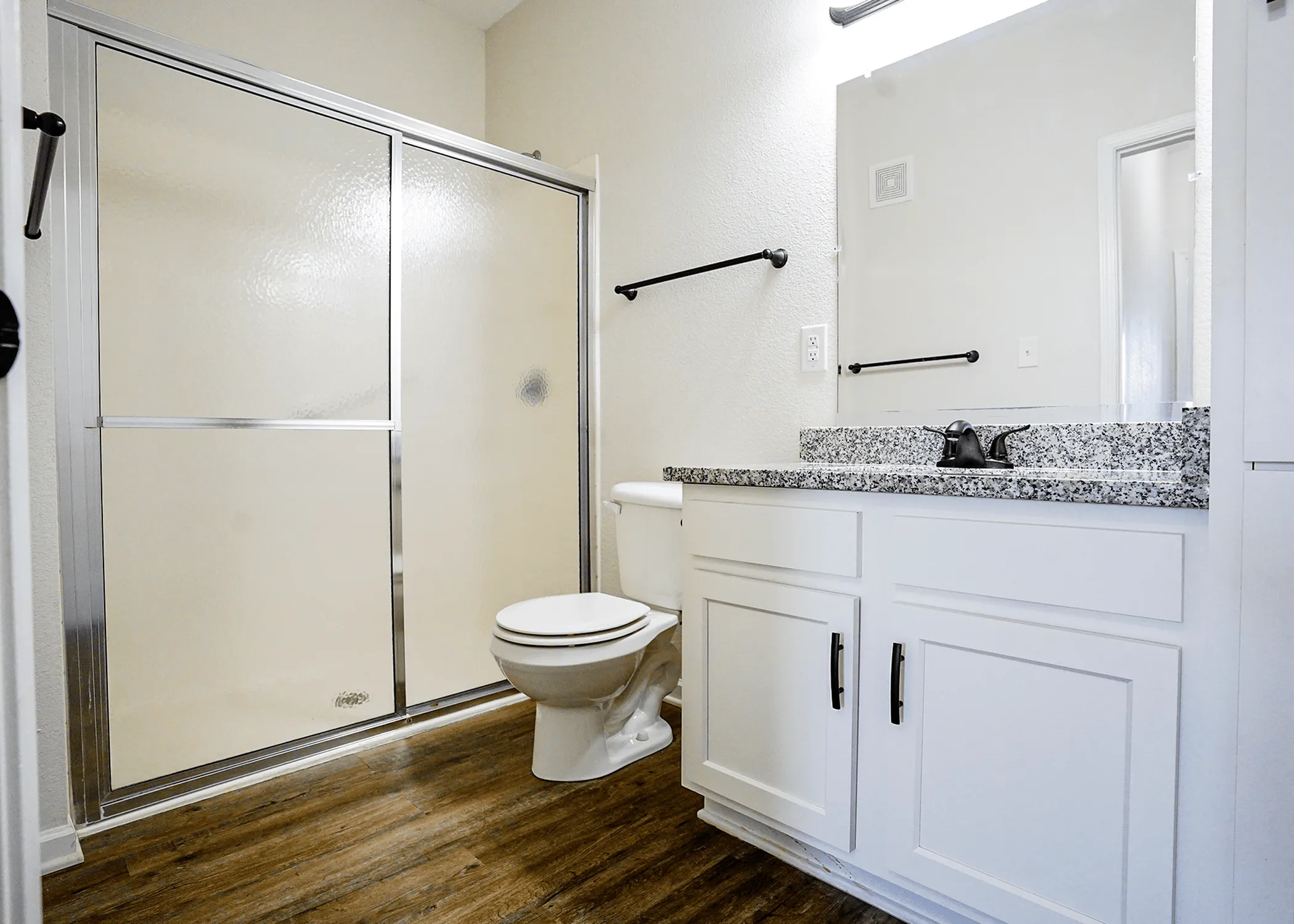 Modern bathroom featuring a sleek shower enclosure, elegant granite countertop, and stylish wood flooring.