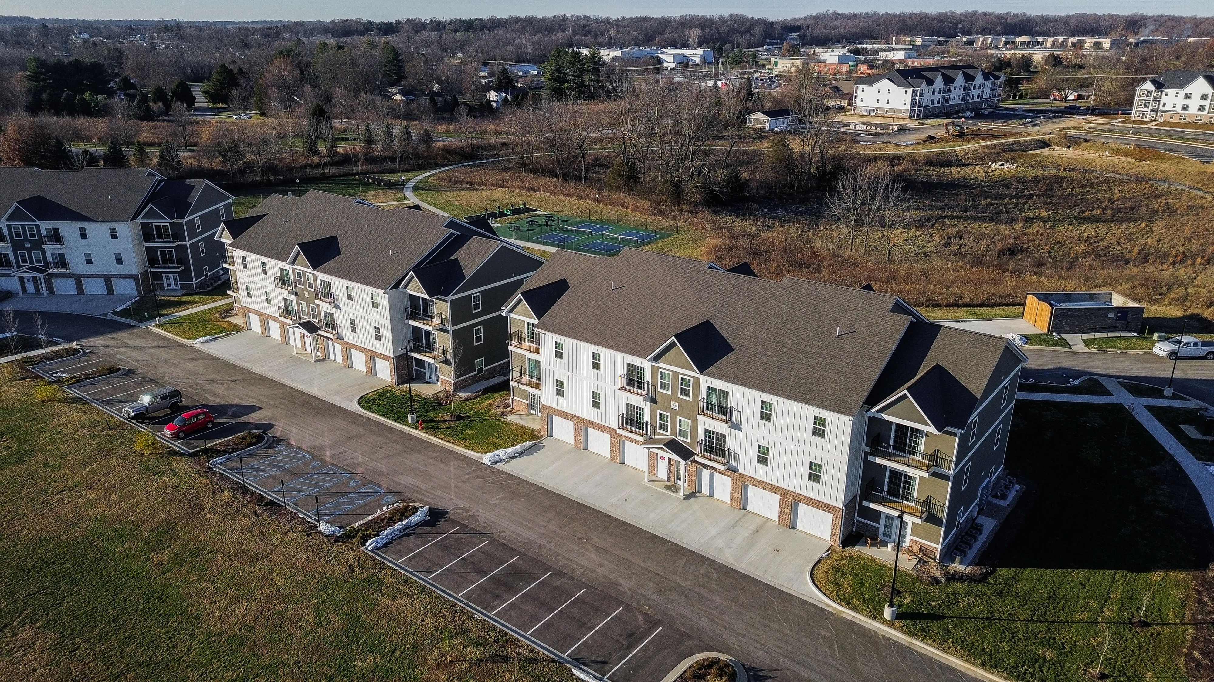 Expansive aerial view of contemporary apartment complex featuring multi-story buildings with private balconies, ample parking, and vibrant surrounding green spaces.