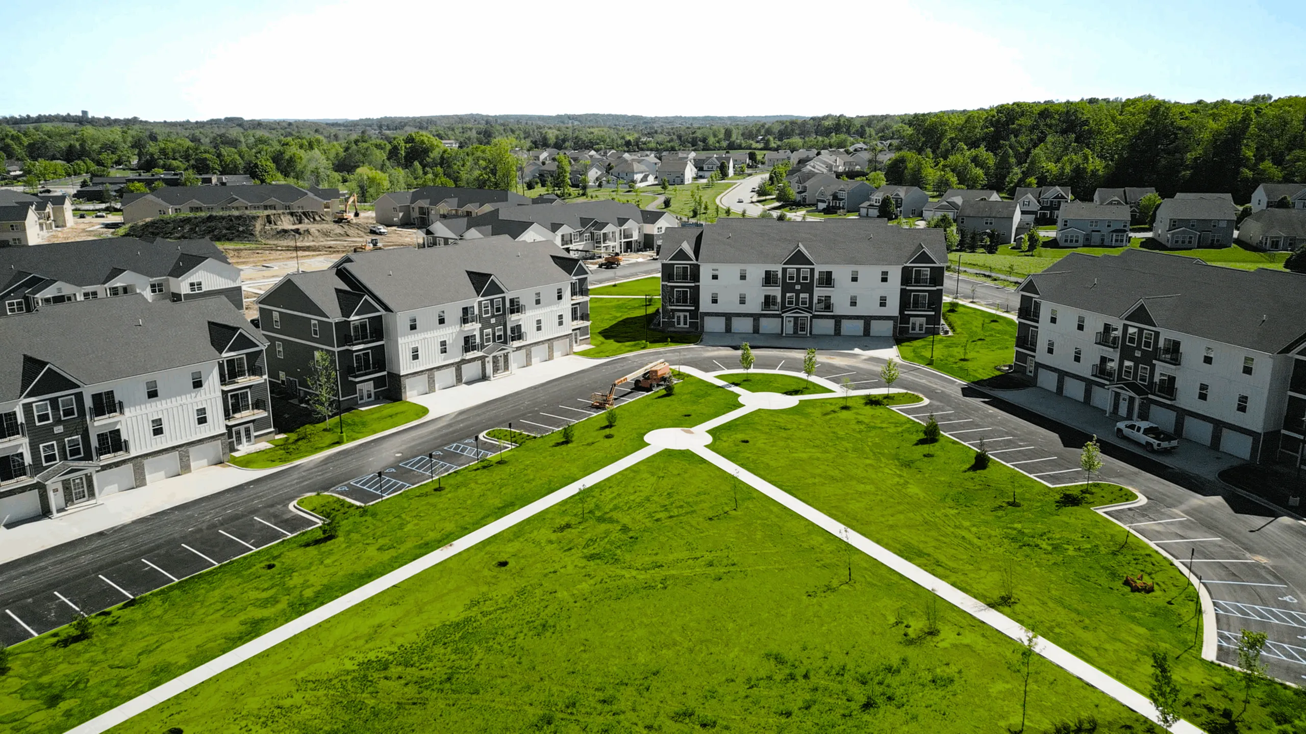 Vibrant aerial view of a modern apartment community surrounded by lush greenery, offering spacious parking and inviting pathways in a serene neighborhood.