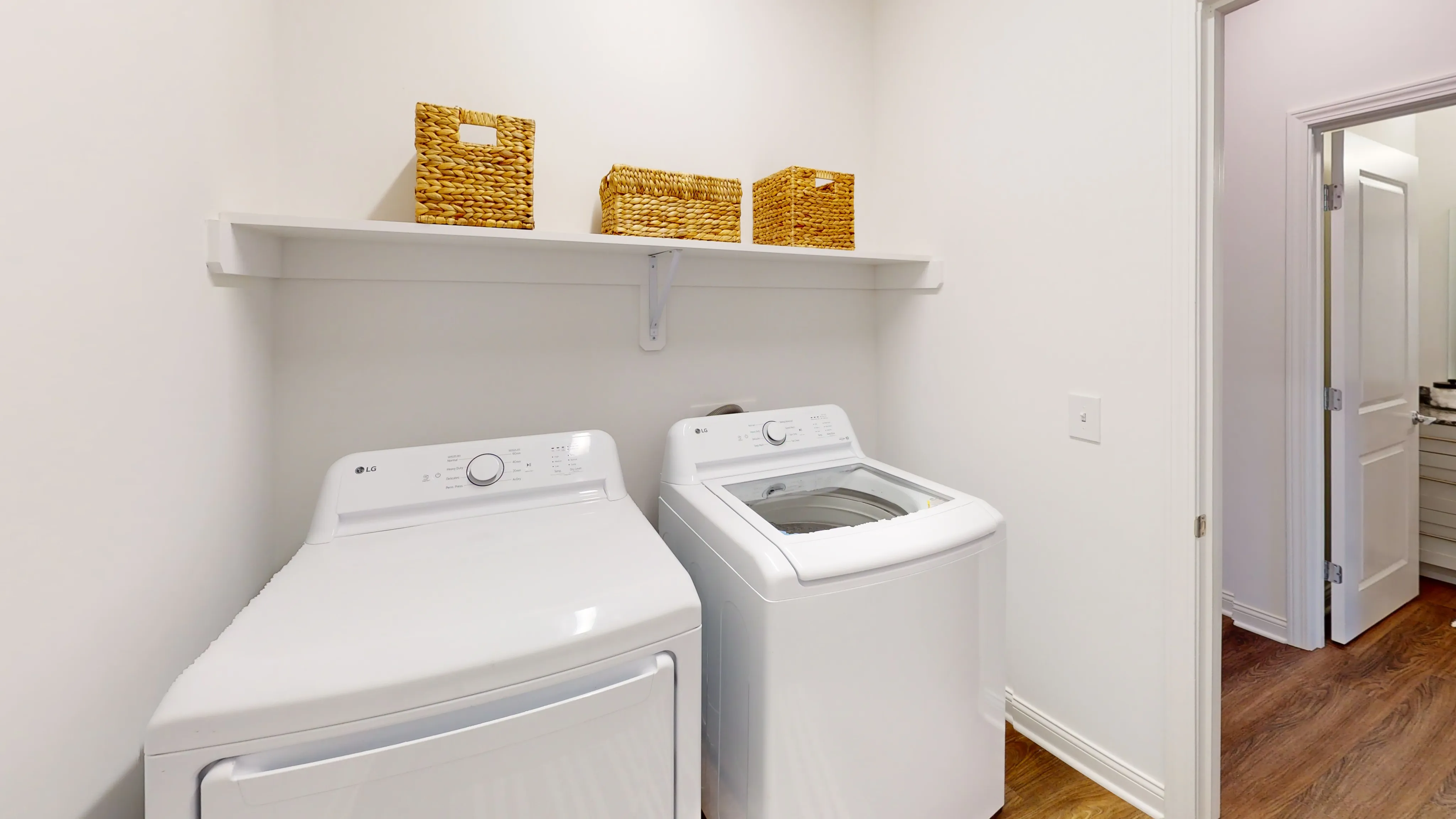 Bright laundry room featuring modern white washer and dryer, elegant wooden flooring, and organized wicker baskets on a sleek shelf.