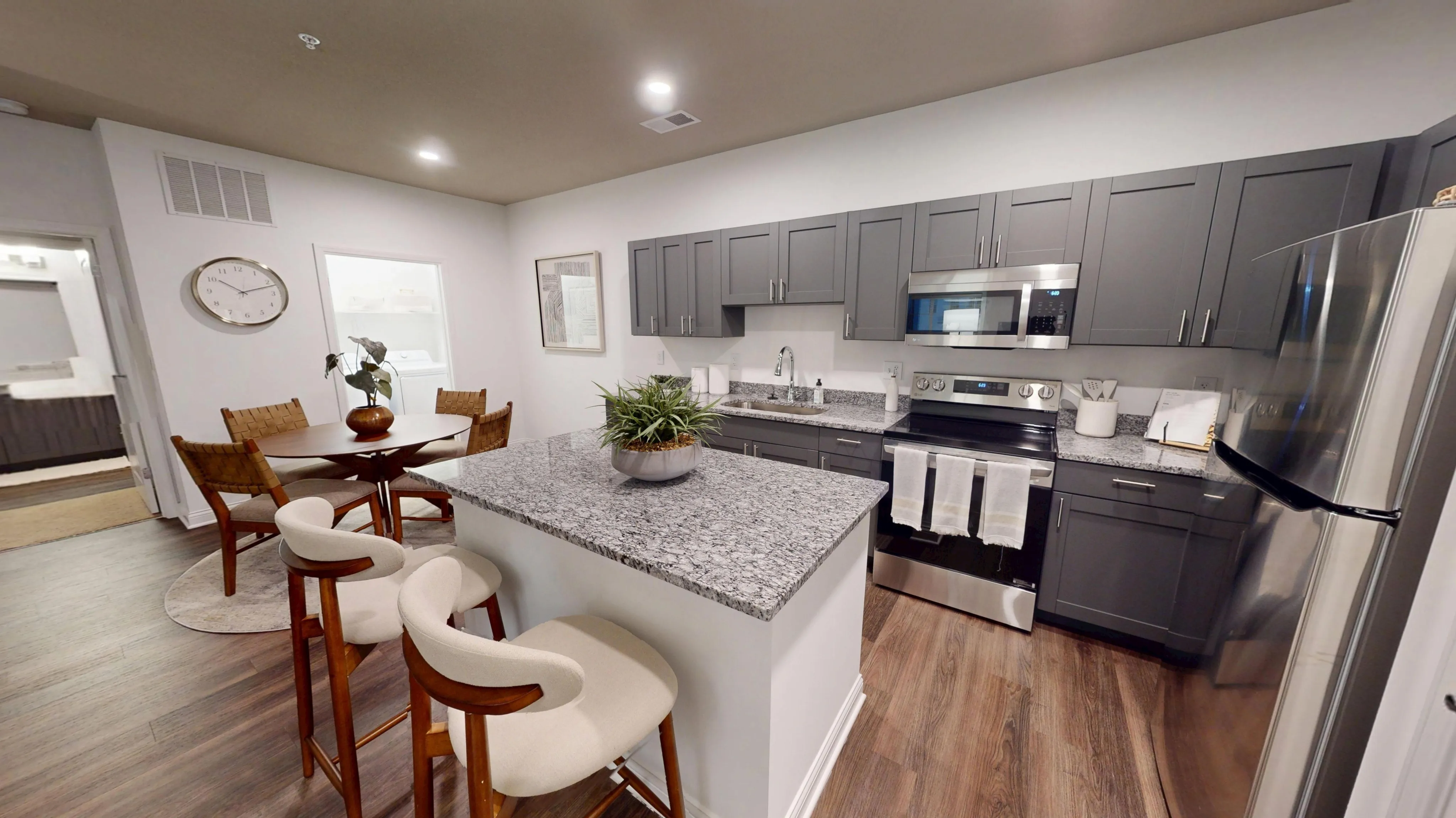 Contemporary kitchen with sleek gray cabinetry, elegant granite countertops, and cozy dining area with stylish chairs on warm wooden flooring.
