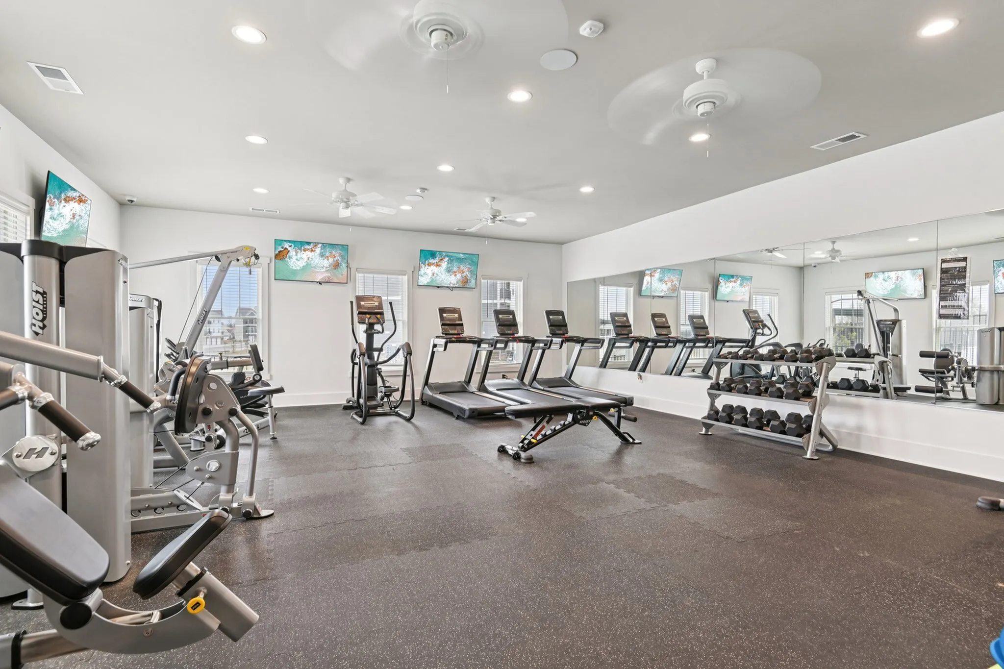 Modern apartment gym equipped with treadmills, weight machines, and free weights, offering a spacious and bright workout environment.
