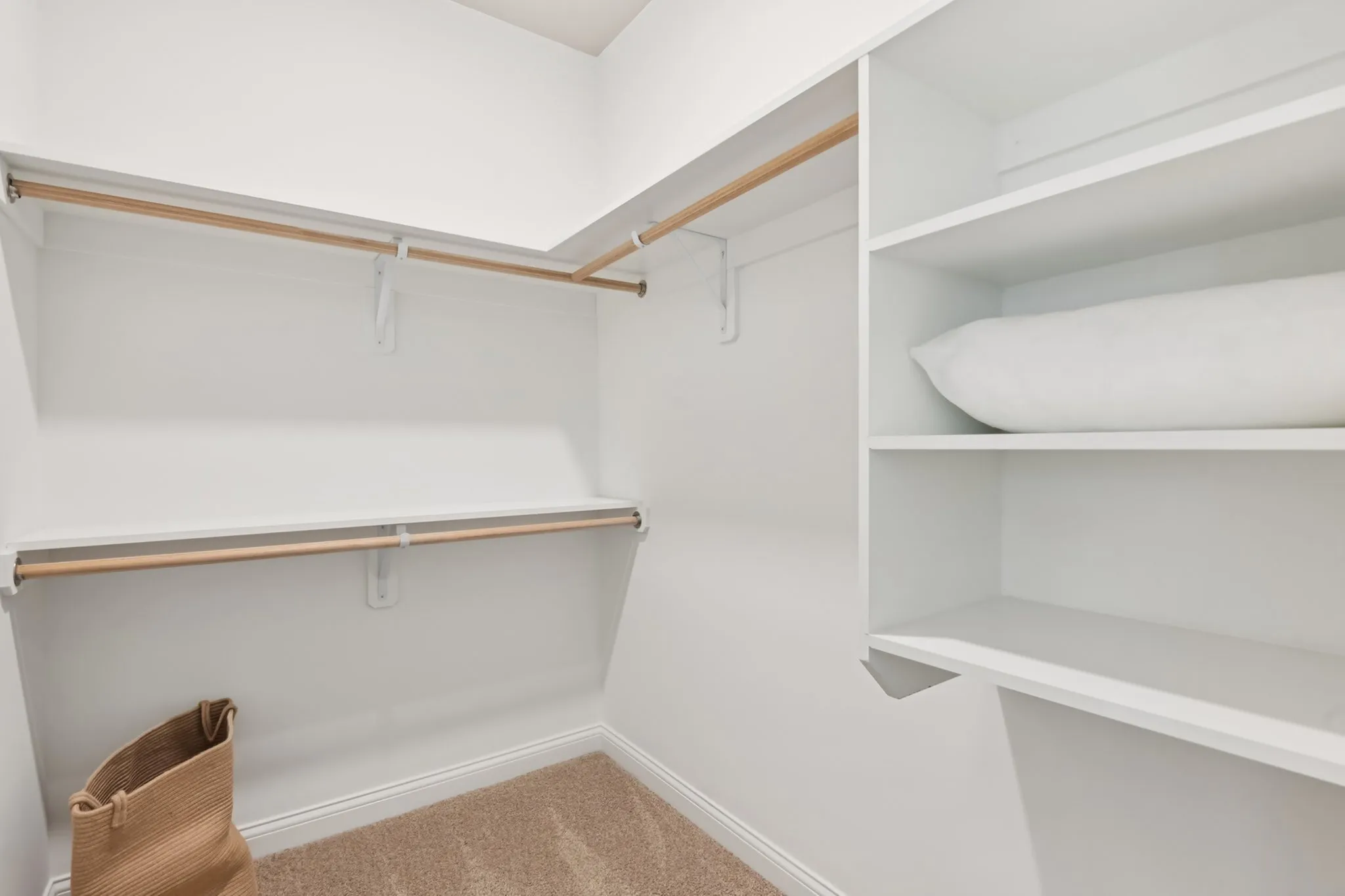 Spacious walk-in closet with elegant shelving and ample storage space, featuring a cozy carpeted floor and a stylish wicker basket.
