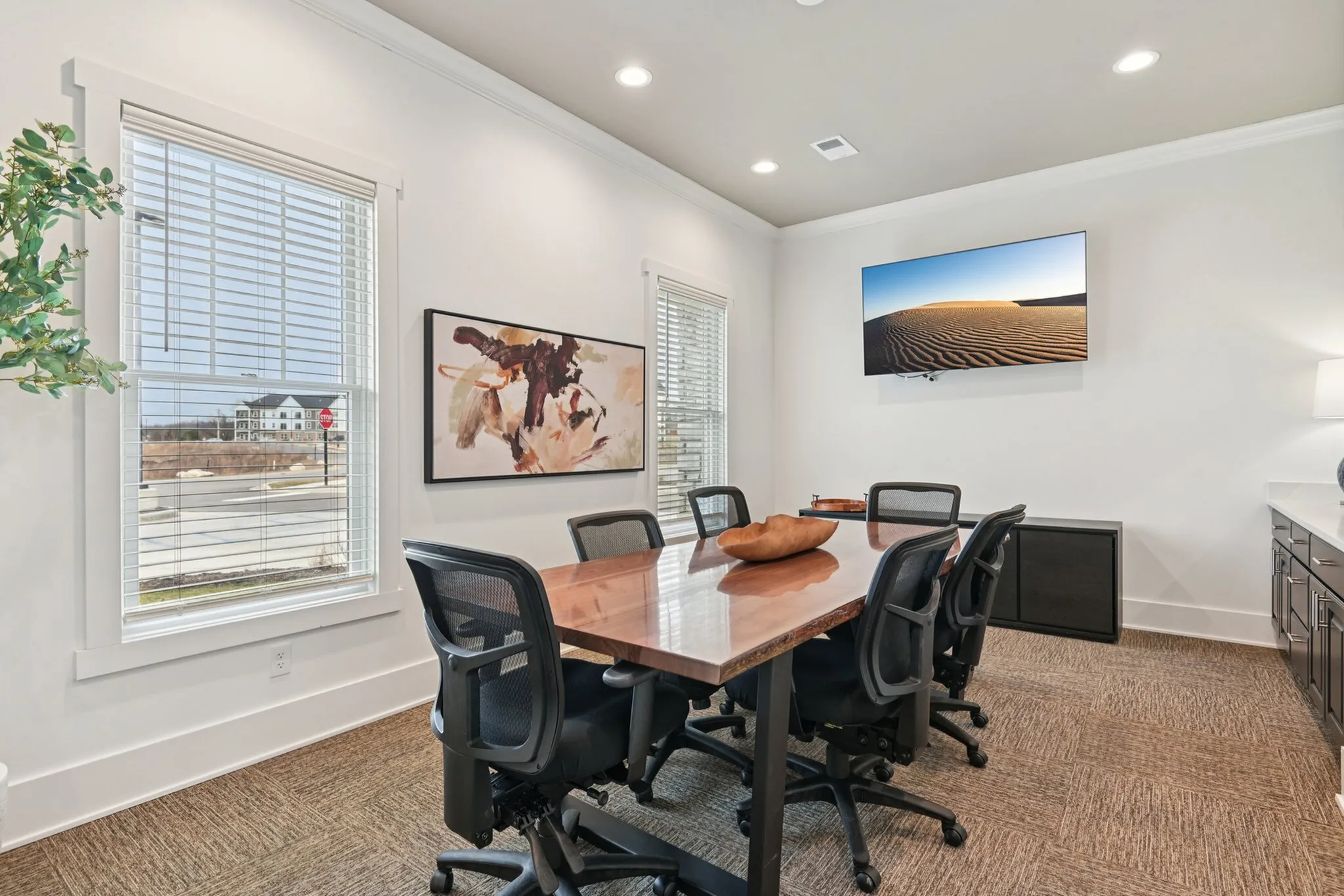 Elegant meeting room with modern decor, featuring a polished wooden table, stylish chairs, and bright natural lighting from large windows.