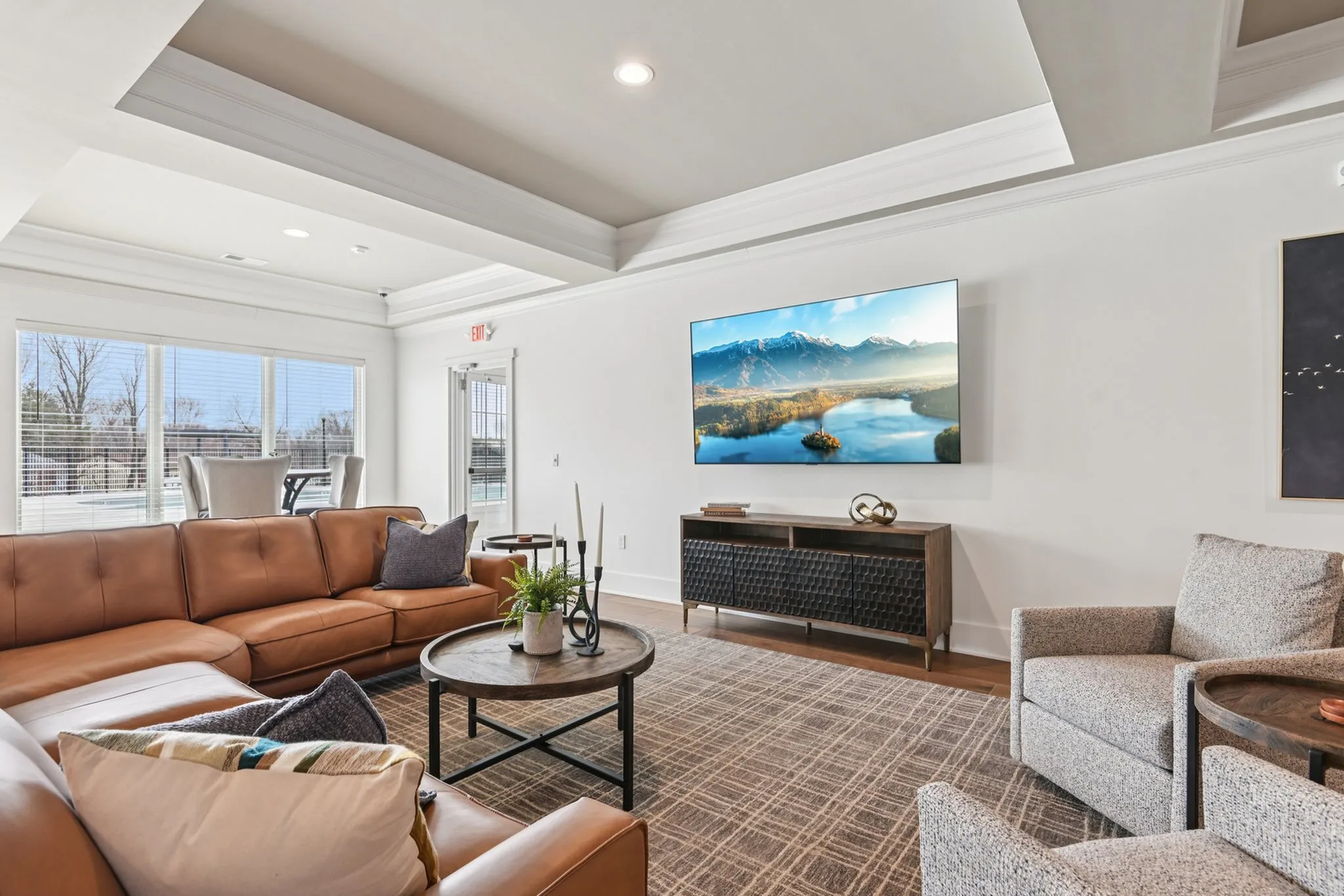 Elegant living room with plush leather sectional, modern decor, mounted flat-screen TV, and large sunlit windows.
