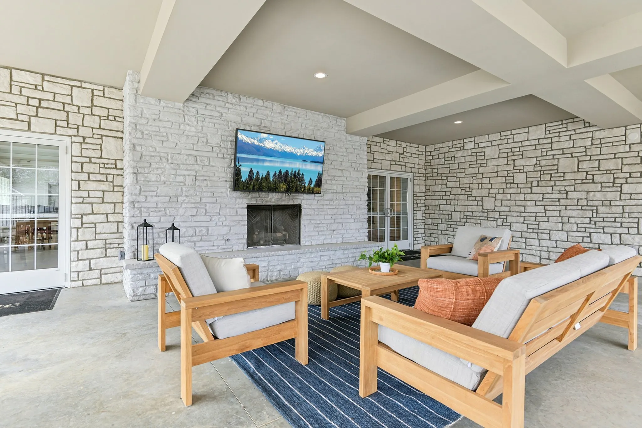 Charming outdoor patio with a cozy seating area, featuring elegant stone walls, a mounted TV, and stylish wooden furniture for perfect relaxation.