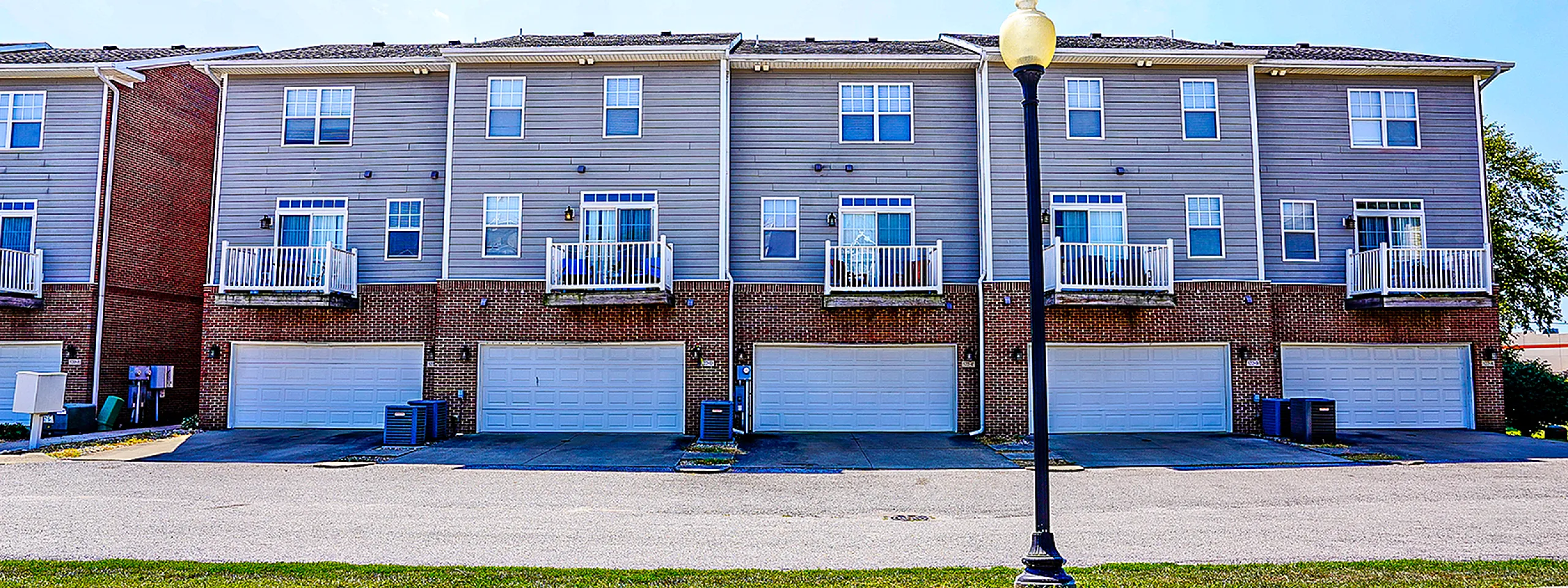 Charming row of modern townhouses with private balconies, spacious garages, and stylish brickwork under a clear blue sky.