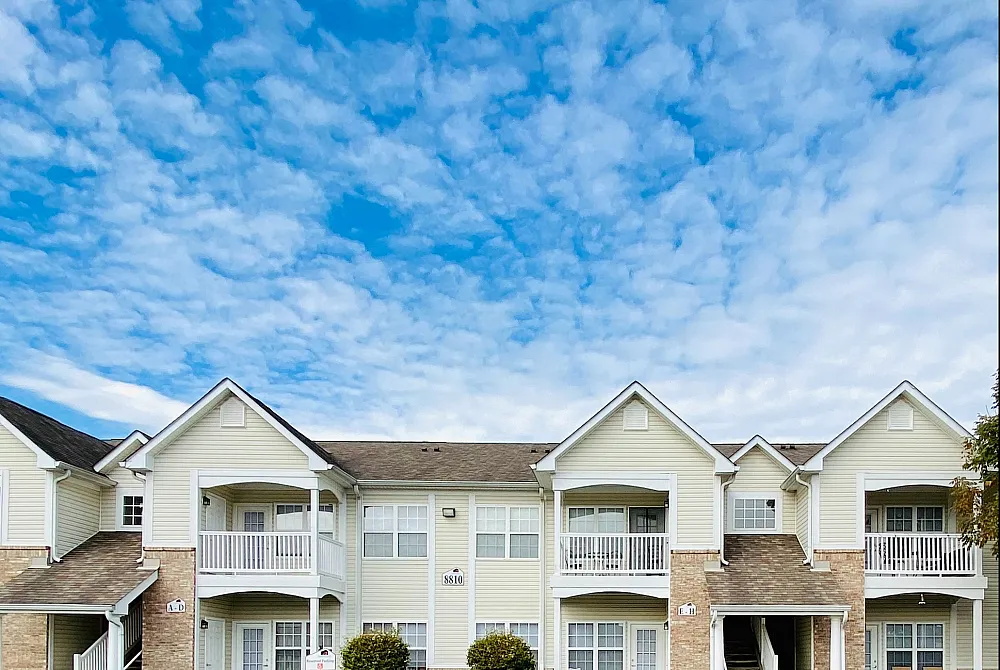 Charming two-story apartment building with spacious balconies and elegant architecture, set under a vibrant blue sky.