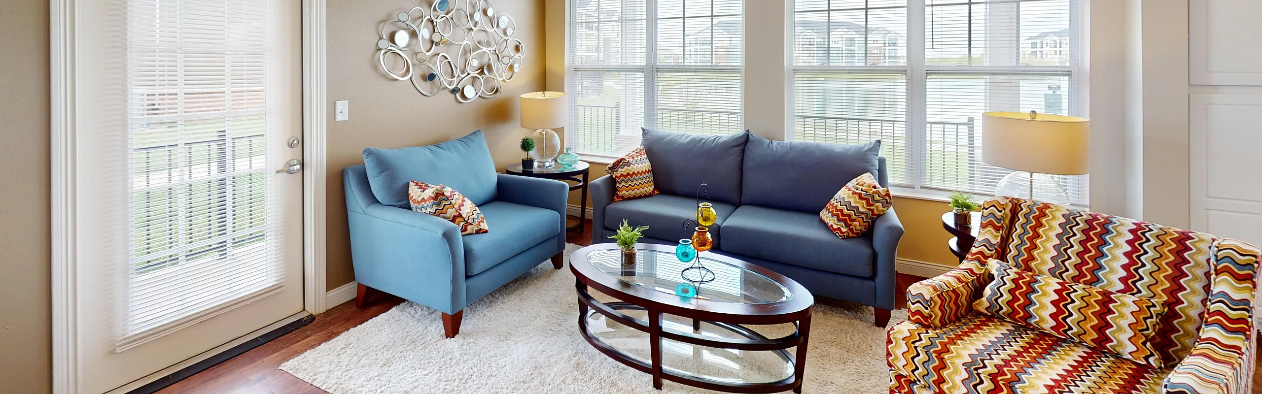 Bright and inviting living room with modern blue furniture, vibrant patterned armchair, and stylish decor, highlighted by large windows and natural light.