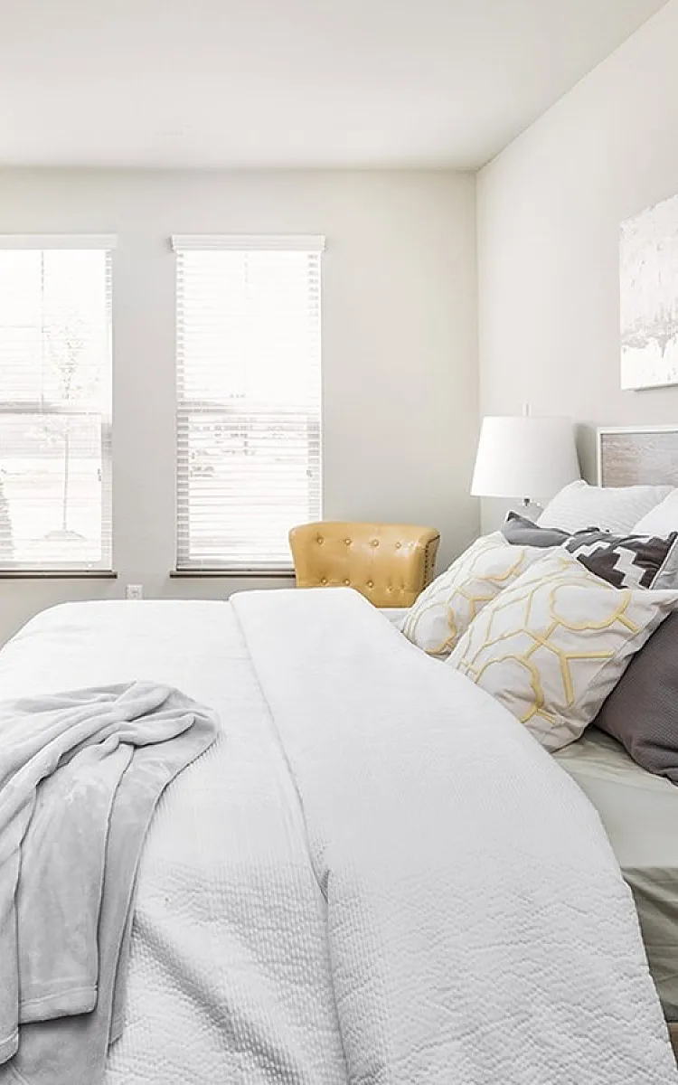 Bright and inviting bedroom with stylish decor, featuring a cozy bed with plush pillows, a chic dresser, and elegant artwork.