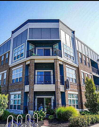 Modern apartment complex featuring elegant brick facade, large windows, and private balconies surrounded by lush greenery, offering a vibrant community living experience.