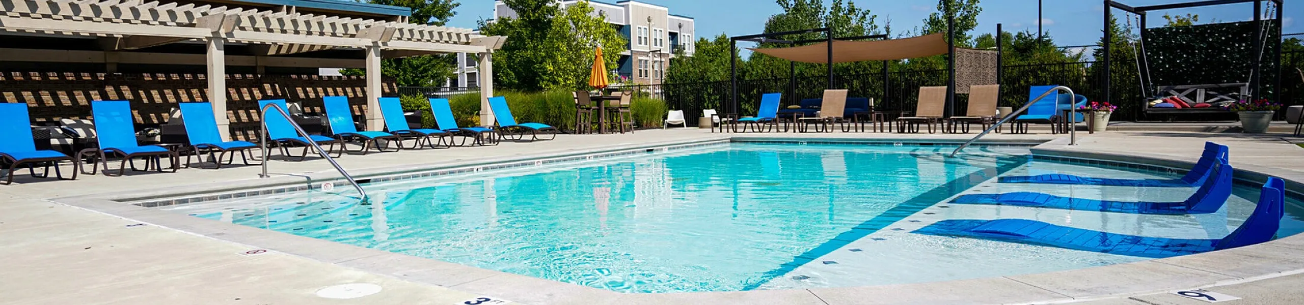 Inviting outdoor pool area with modern lounge chairs and shaded pergola, perfect for relaxing under a clear blue sky.