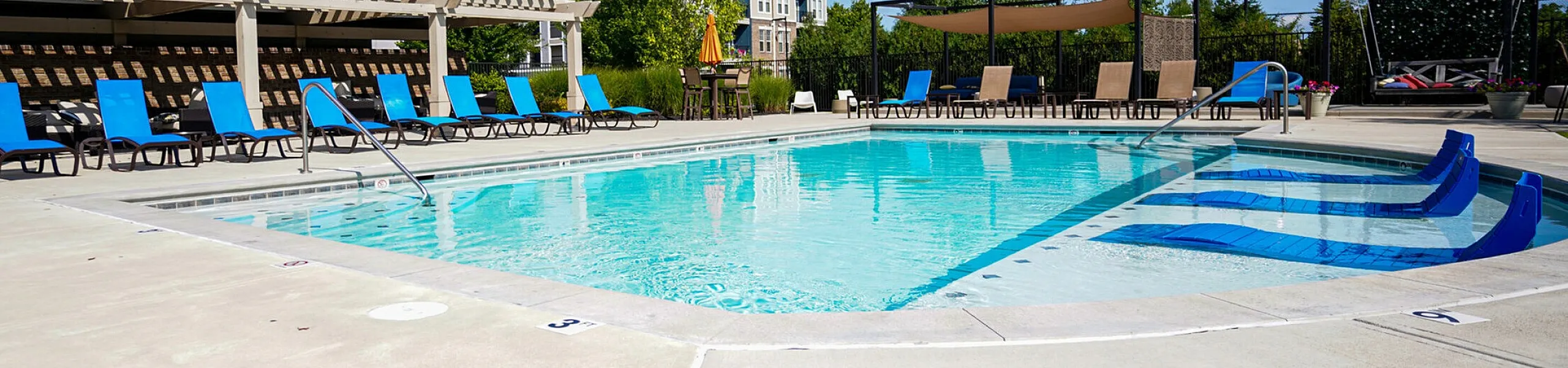 Inviting outdoor pool area with modern lounge chairs and shaded pergolas, surrounded by vibrant greenery and stylish apartment buildings.