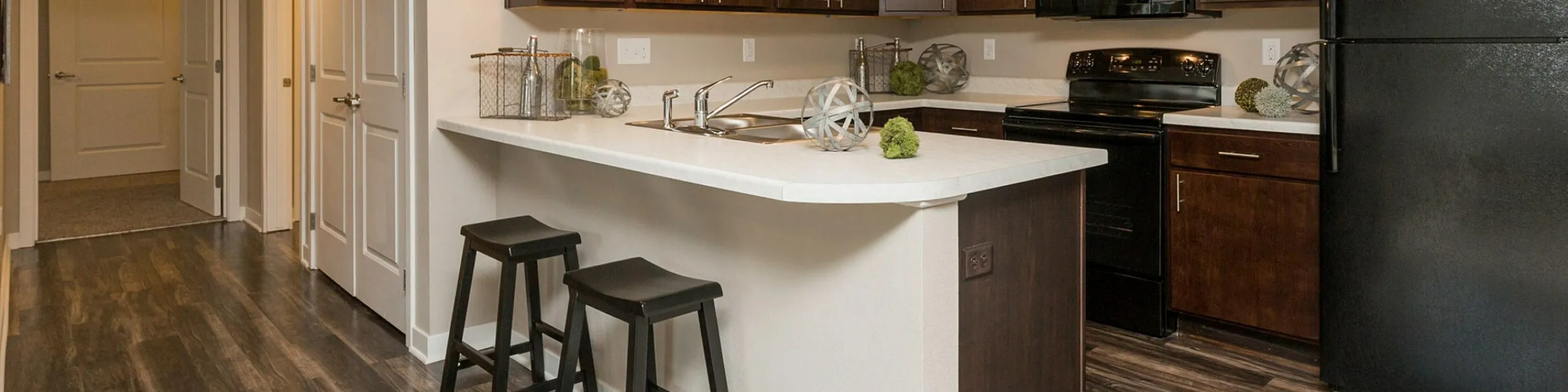 Modern kitchen with sleek dark cabinets, a spacious island with bar stools, and elegant lighting in a stylish apartment setting.