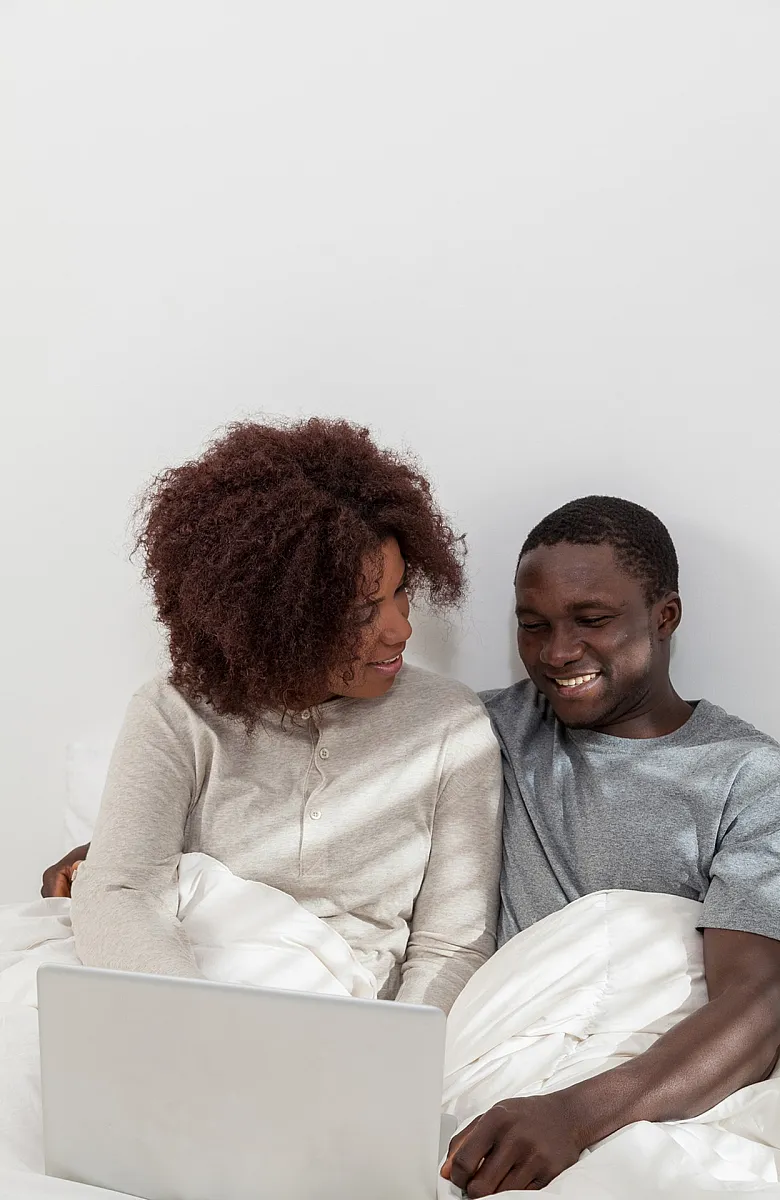 Happy couple relaxing and using a laptop together, creating a cozy and inviting atmosphere in a bright and modern bedroom.
