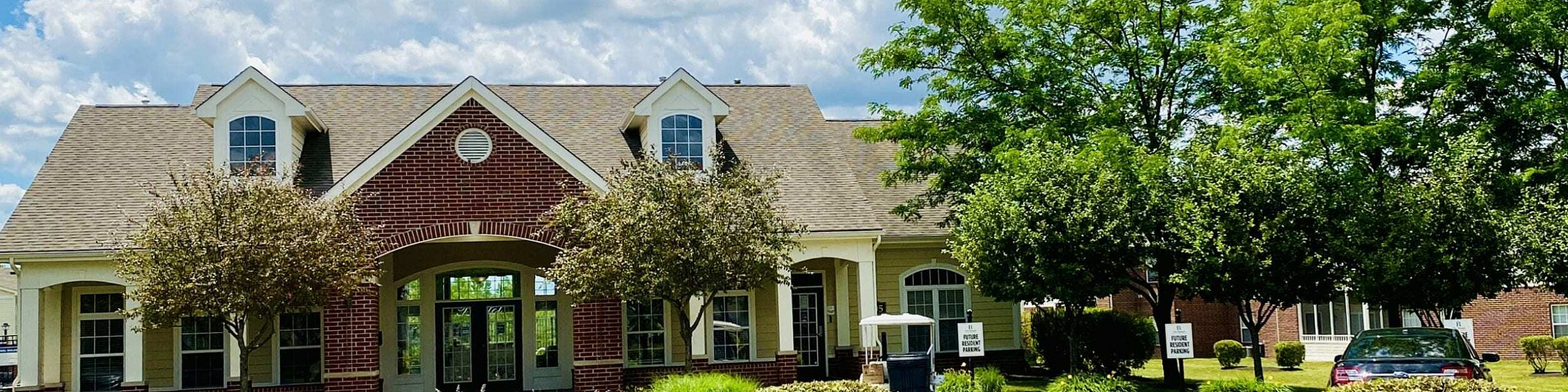 Inviting suburban property with charming brick facade, surrounded by lush greenery and vibrant landscaping under a bright, blue sky.
