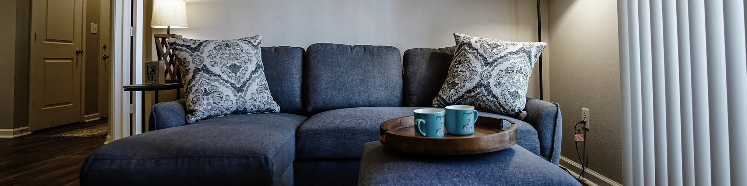 Inviting living room with a cozy sectional sofa, elegant floor lamp, and serene forest artwork, perfect for relaxation.