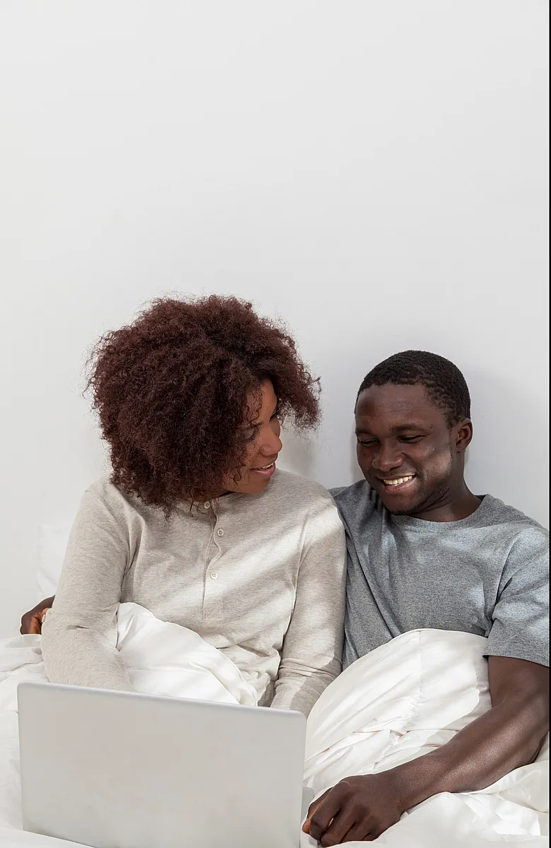 Smiling couple sitting close together in bed on a laptop.