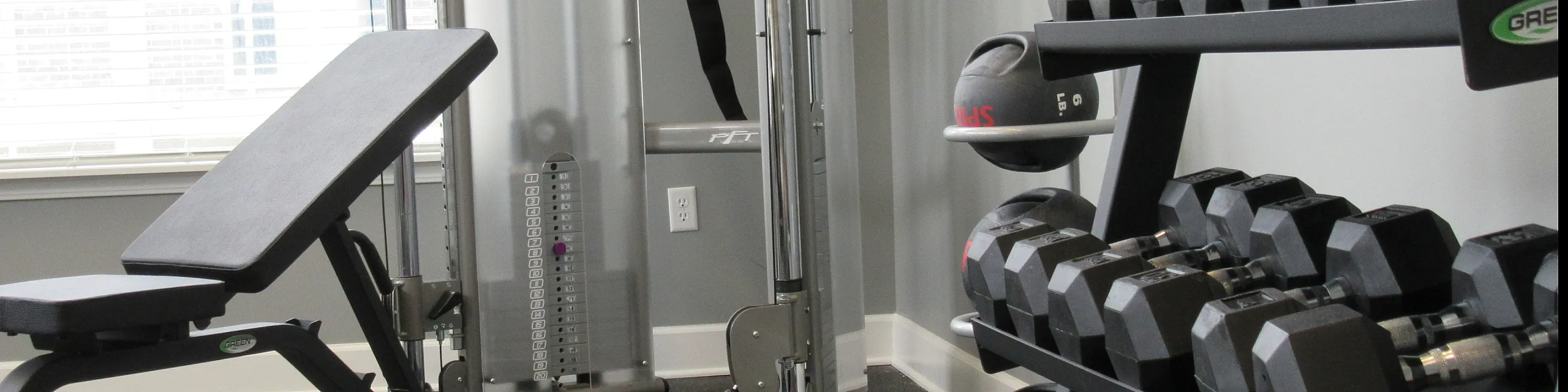 Modern apartment gym with state-of-the-art equipment, including a sleek adjustable bench, advanced weight machines, and a full set of dumbbells for diverse workouts.