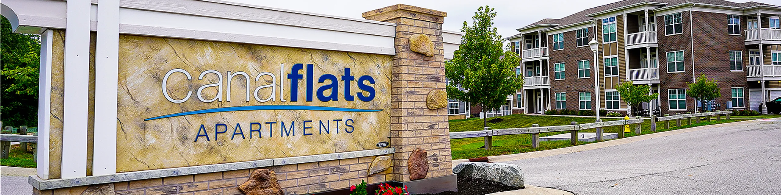 Charming Canal Flats Apartments sign with landscaped entrance, showcasing modern brick buildings and lush greenery in a serene setting.