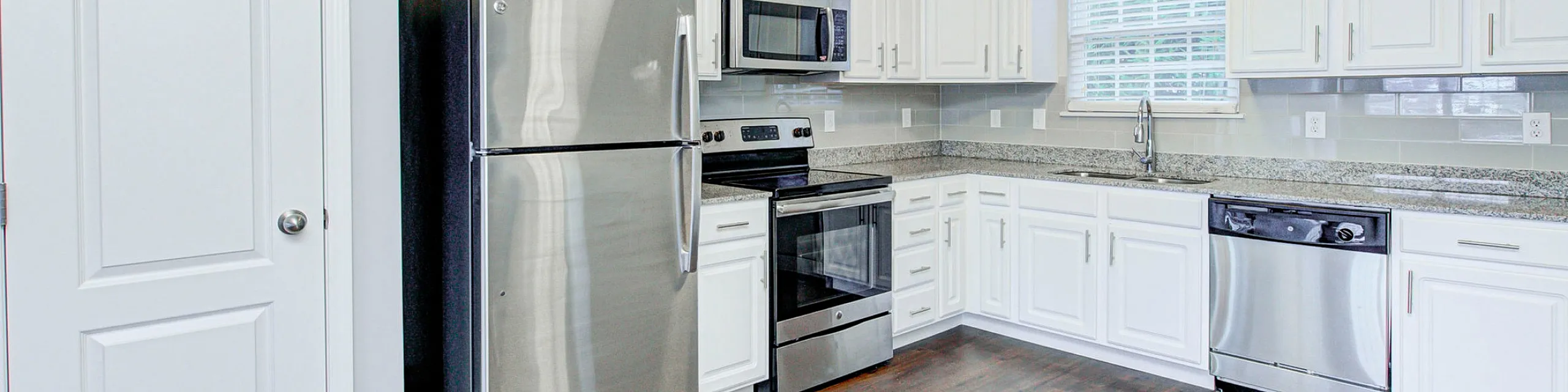 Modern kitchen featuring sleek stainless steel appliances, elegant granite countertops, and pristine white cabinetry, creating a chic and inviting cooking space.