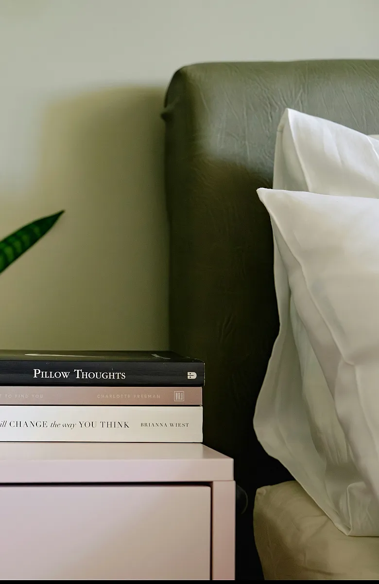 Chic bedside setup with a 'but first, coffee' mug, books, and lively greenery, creating a cozy bedroom vibe.