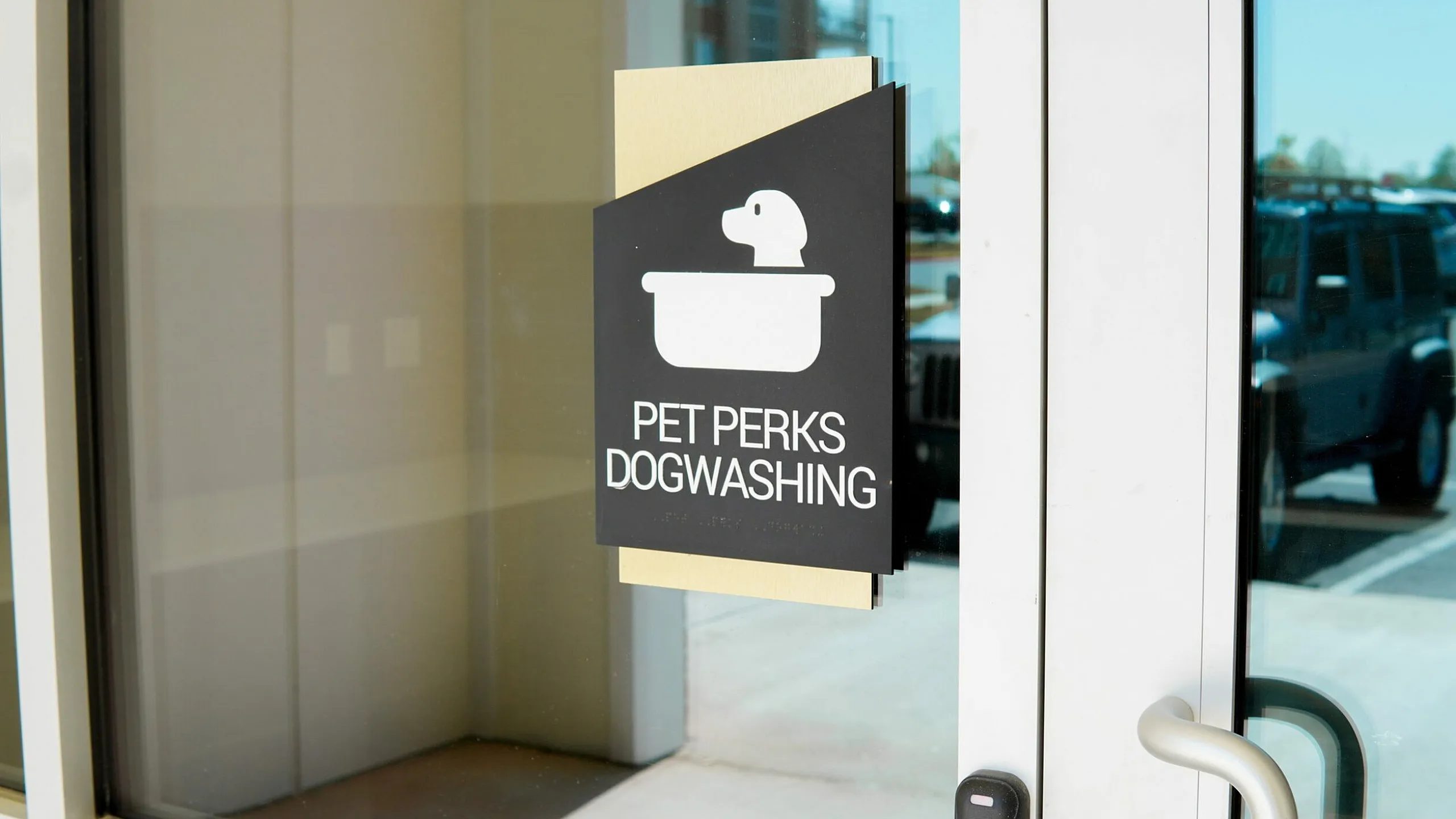 Inviting pet-friendly apartment amenity featuring 'Pet Perks Dog Washing' sign on a sunny glass door, complete with modern convenience.