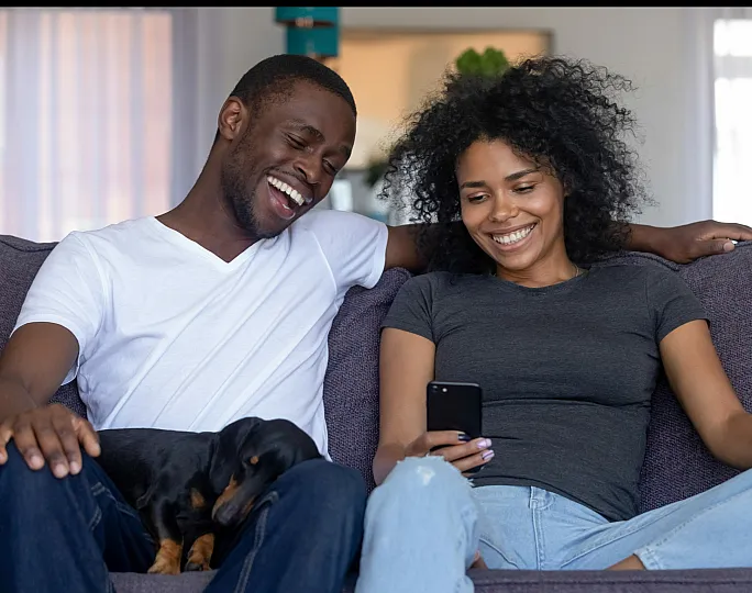 Joyful couple relaxing on a cozy sofa, enjoying quality time with their pet dog in a bright and inviting living room.