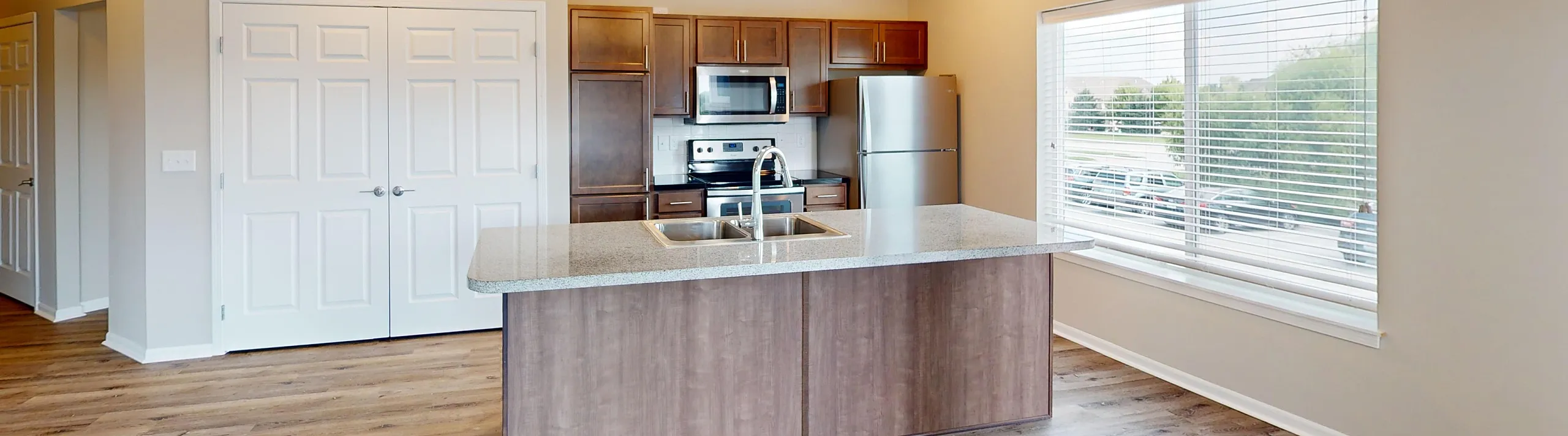 Modern kitchen with sleek dark wood cabinets, stainless steel appliances, and a stylish island with granite countertops. The space is brightened by large windows and warm wood flooring, creating a welcoming and contemporary atmosphere.