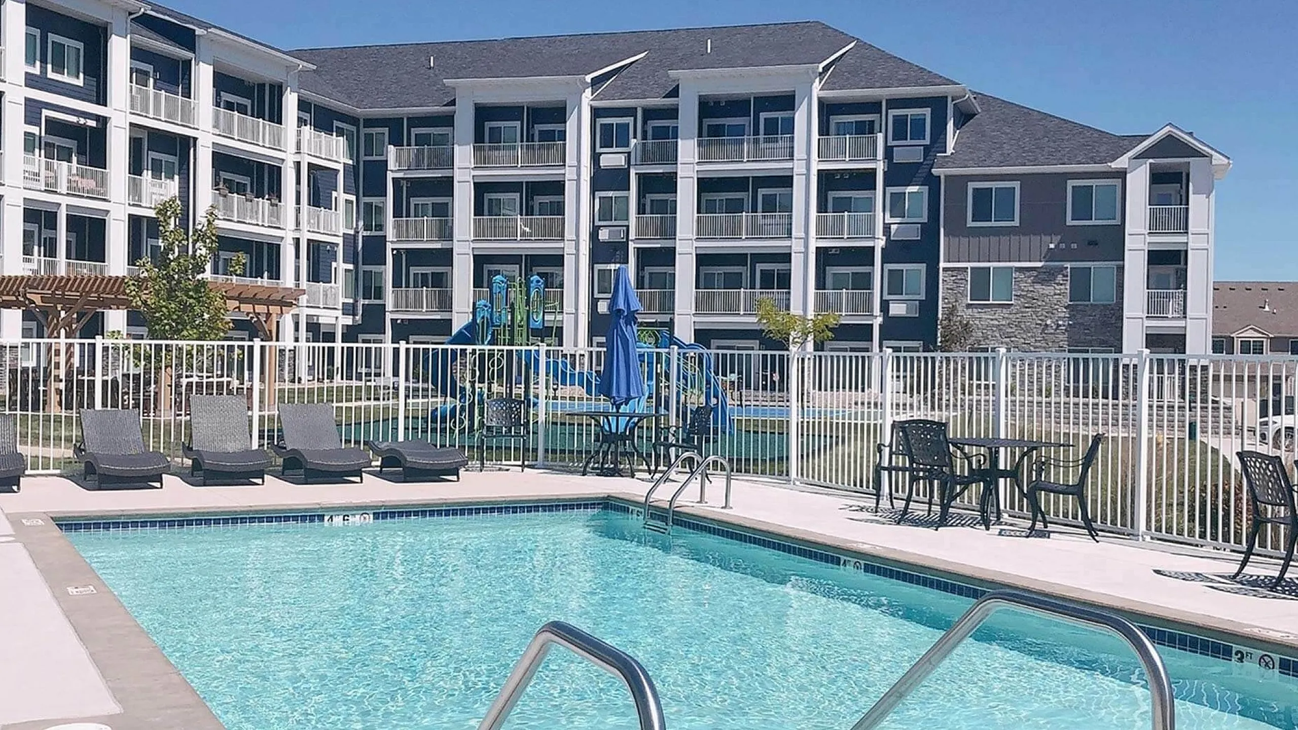 Modern apartment complex featuring a large swimming pool, surrounded by stylish loungers and vibrant outdoor seating, perfect for relaxation and leisure.