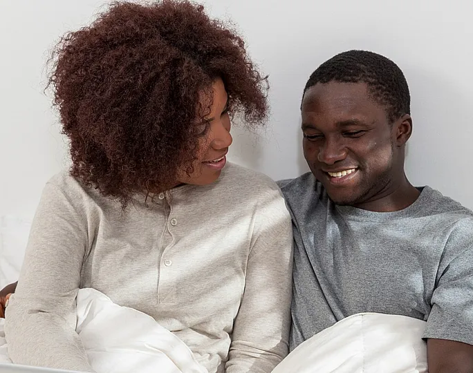 Happy couple relaxing in a cozy bedroom while browsing the internet on a laptop, showcasing a serene and inviting living space.