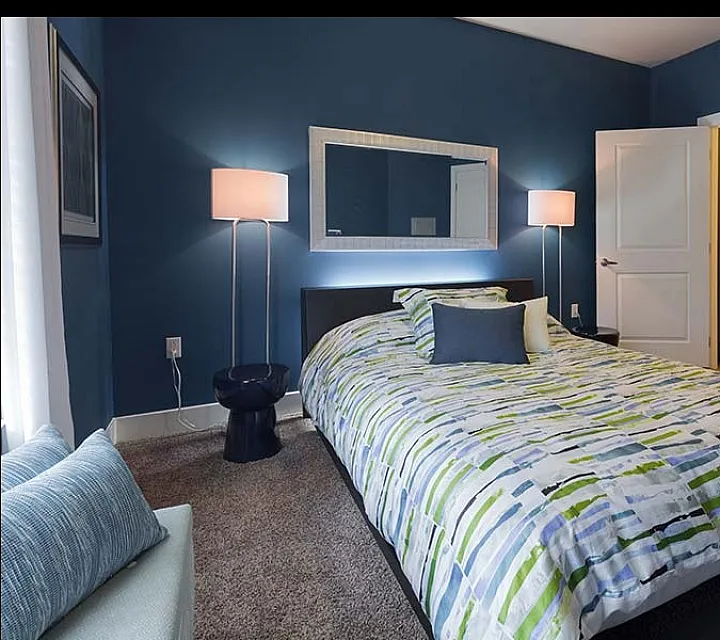Chic and cozy bedroom with stylish blue walls, modern lamps, and a plush bedspread, creating a serene retreat adjacent to a luxurious bathroom.